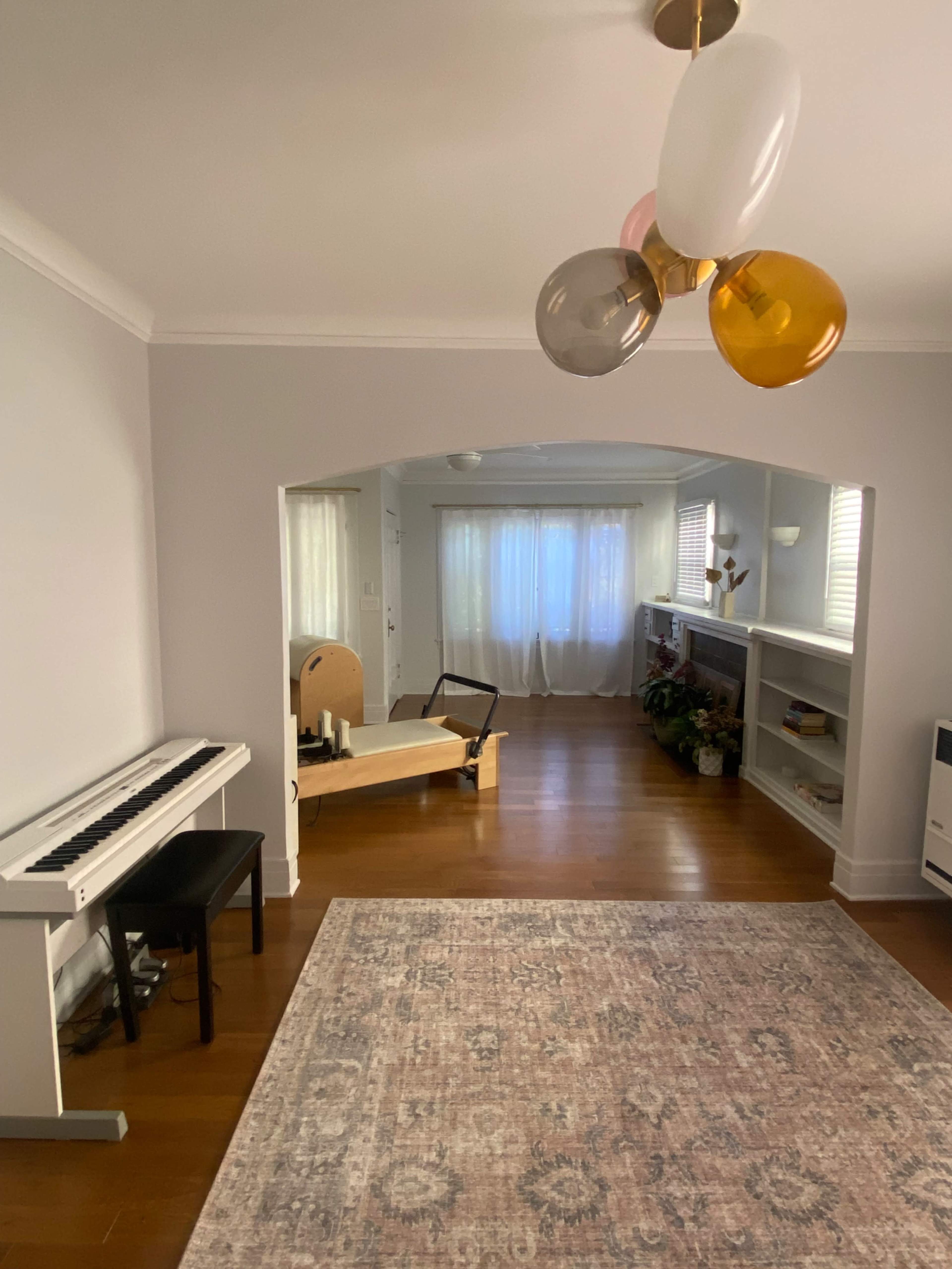 A spacious living area features a piano, a decorative rug, and a light-filled room with a minimalist seating arrangement.