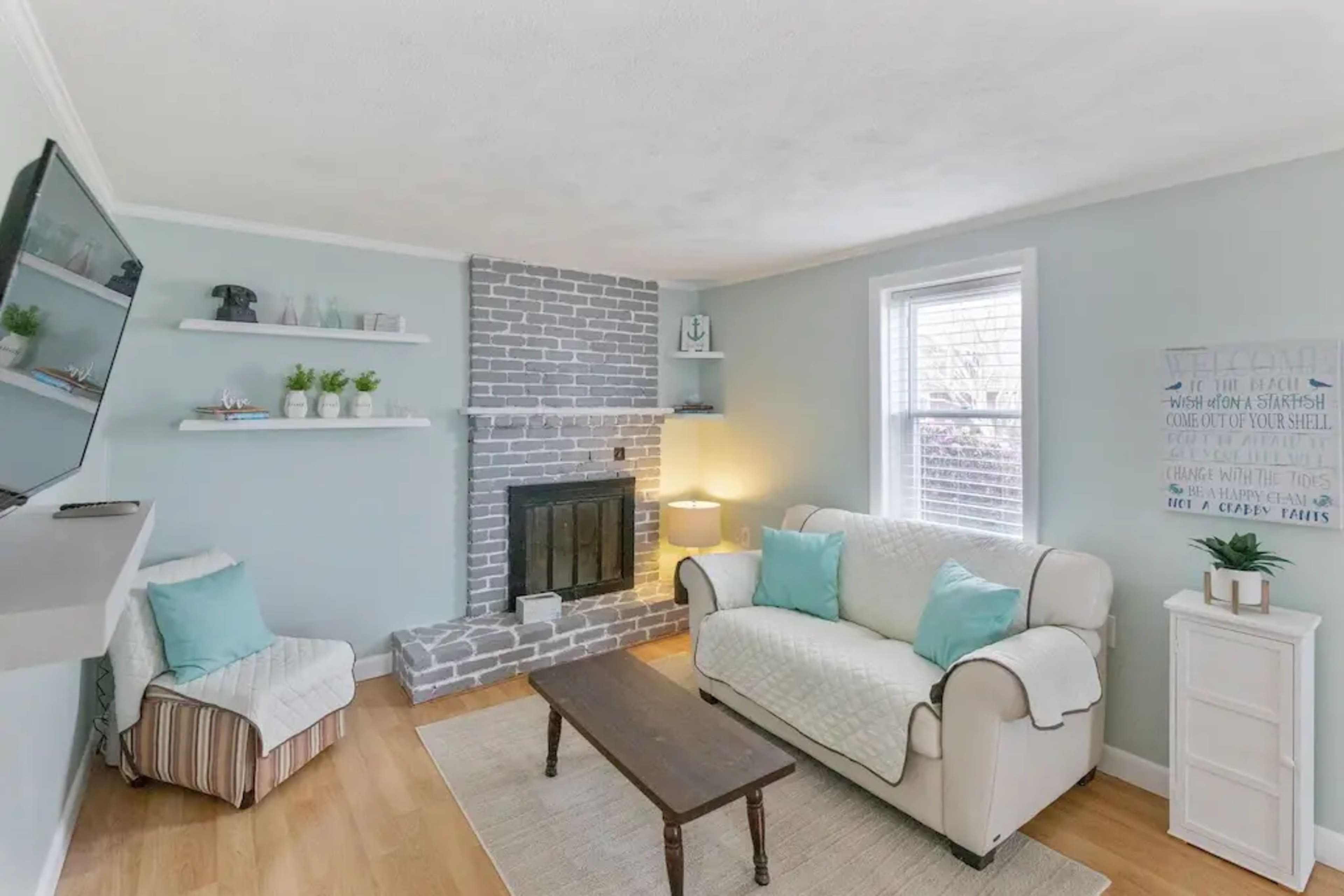 A small living room with a light blue color scheme, featuring a gray brick fireplace, a comfortable sofa, and a wooden coffee table.