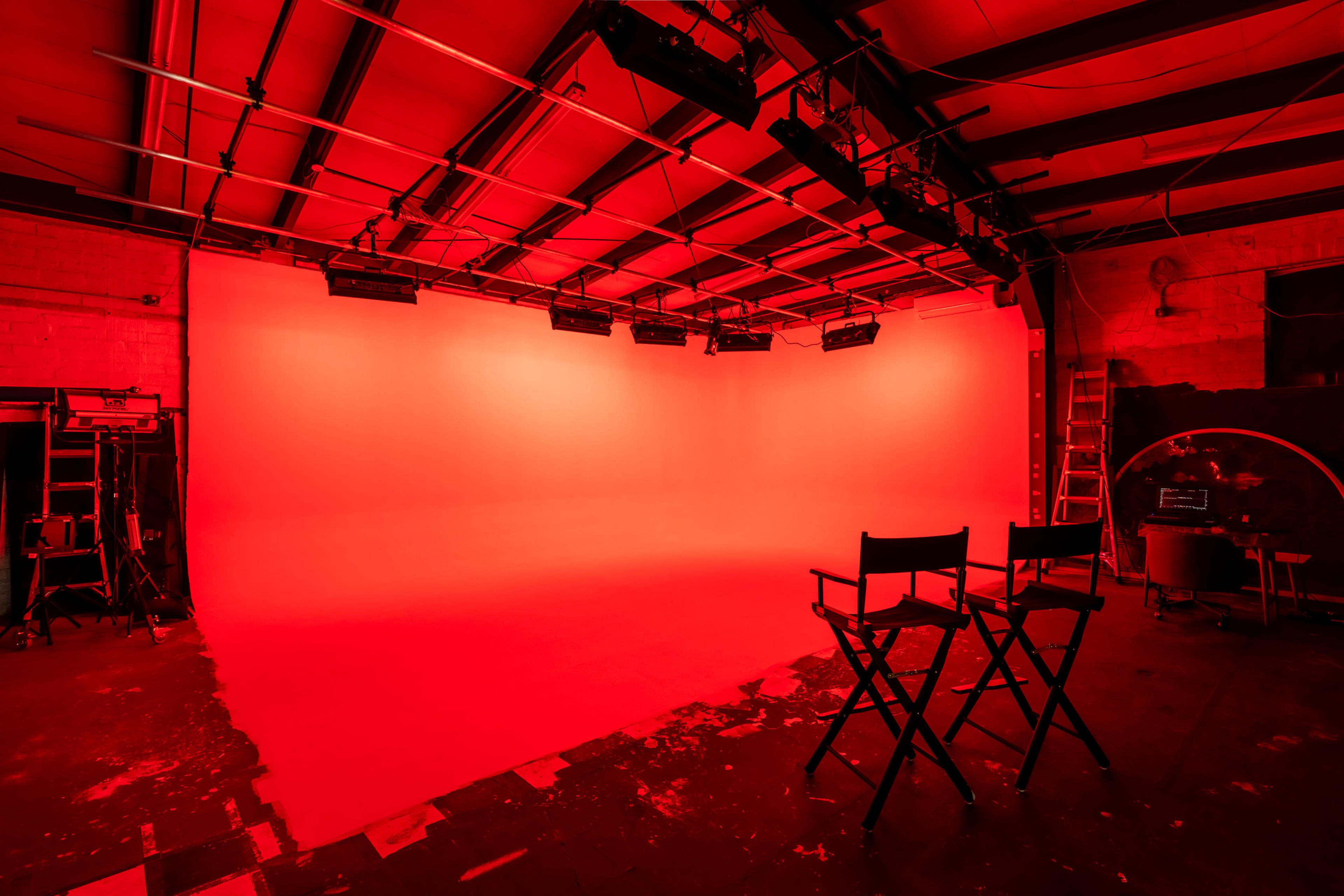 A photography studio features a red backdrop with two empty director's chairs positioned in front of it.