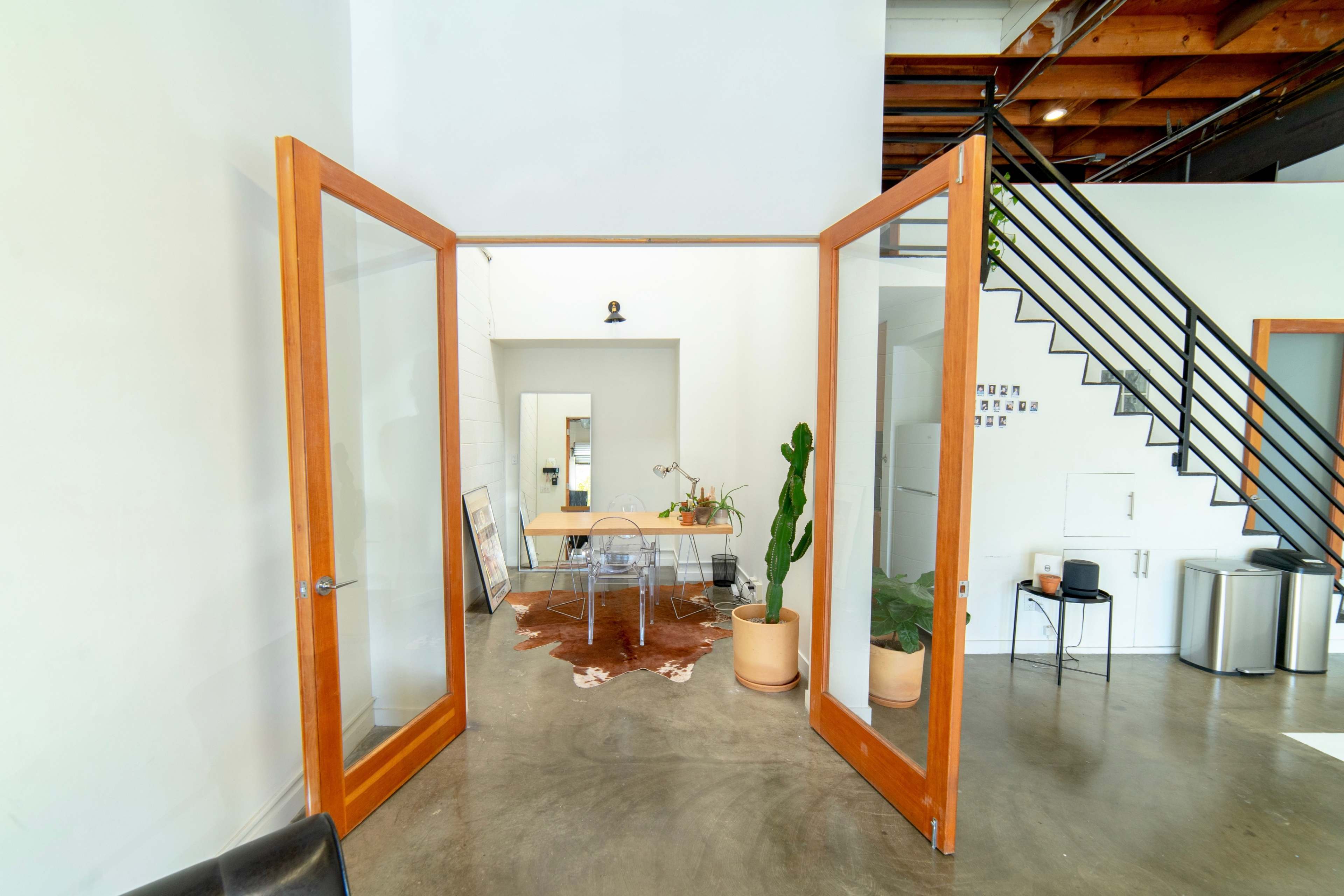 An open double door leading into a bright, minimalist office space with a wooden table and plants.