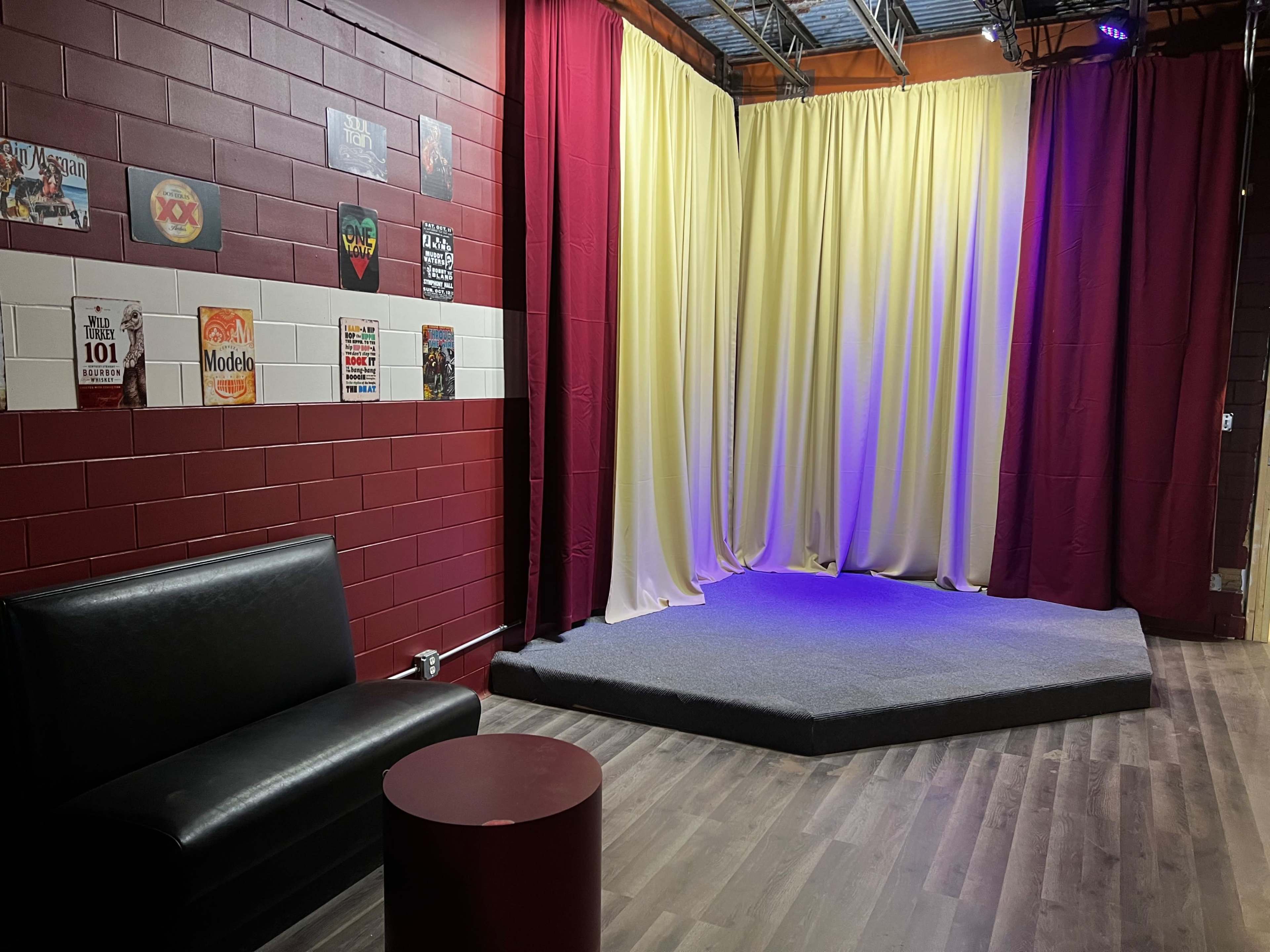 A small stage with draped curtains, accompanied by a black couch and a round table in a corner of a room.