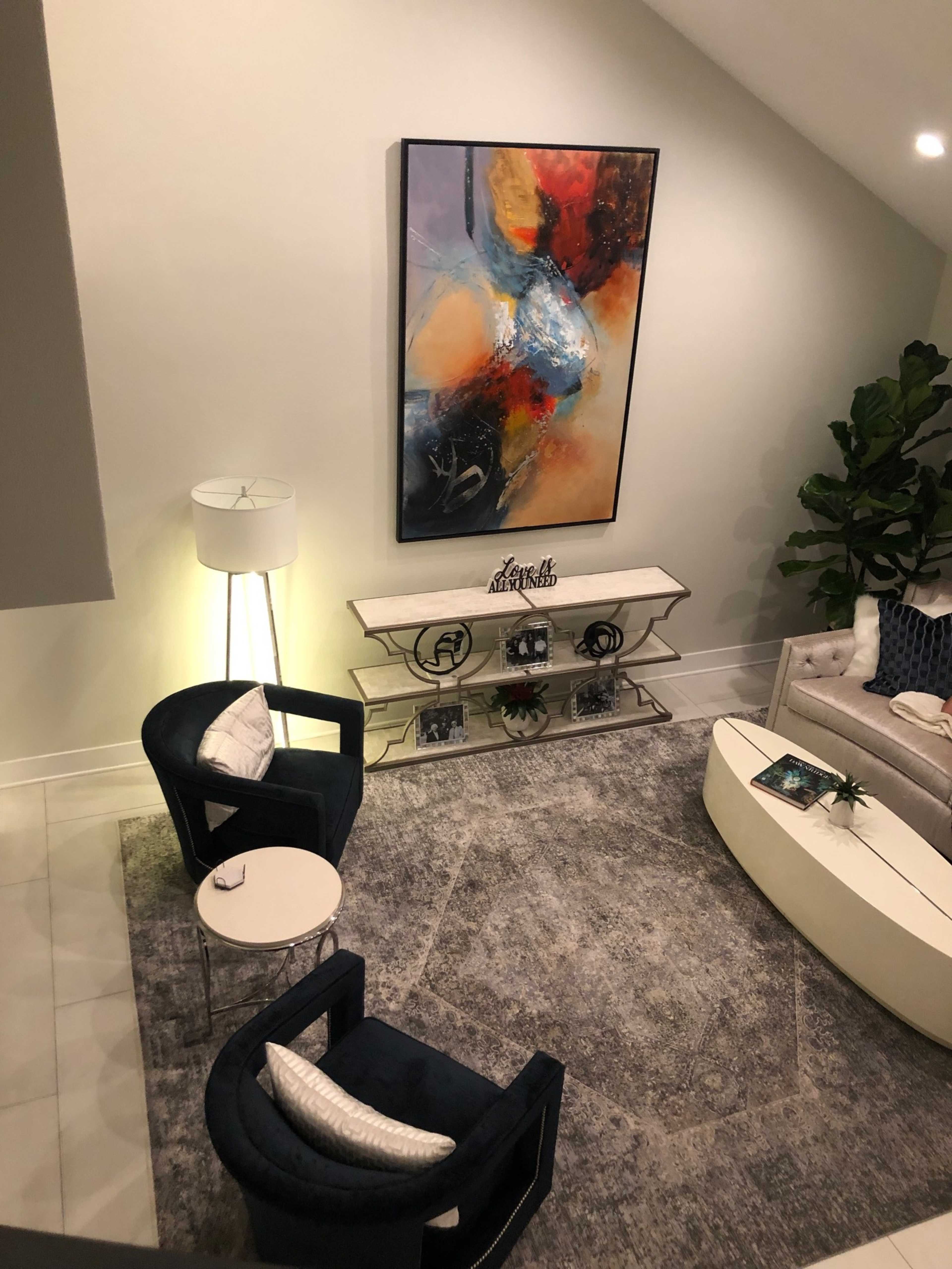 The image shows a modern living room with two blue chairs, a coffee table, and a white sofa, featuring a large abstract painting on the wall.