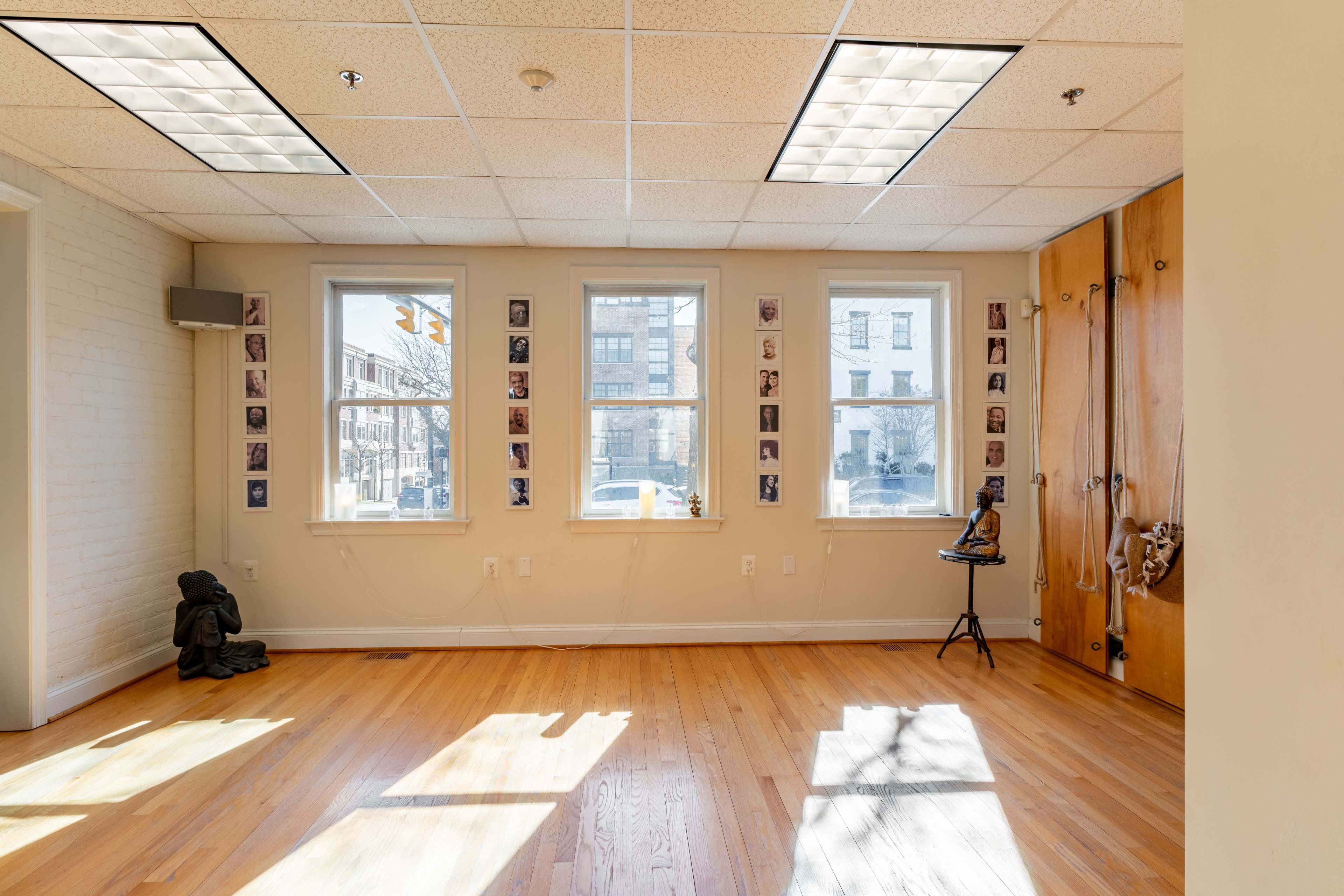 A bright, spacious room with large windows, wooden floors, and photos arranged on the walls.