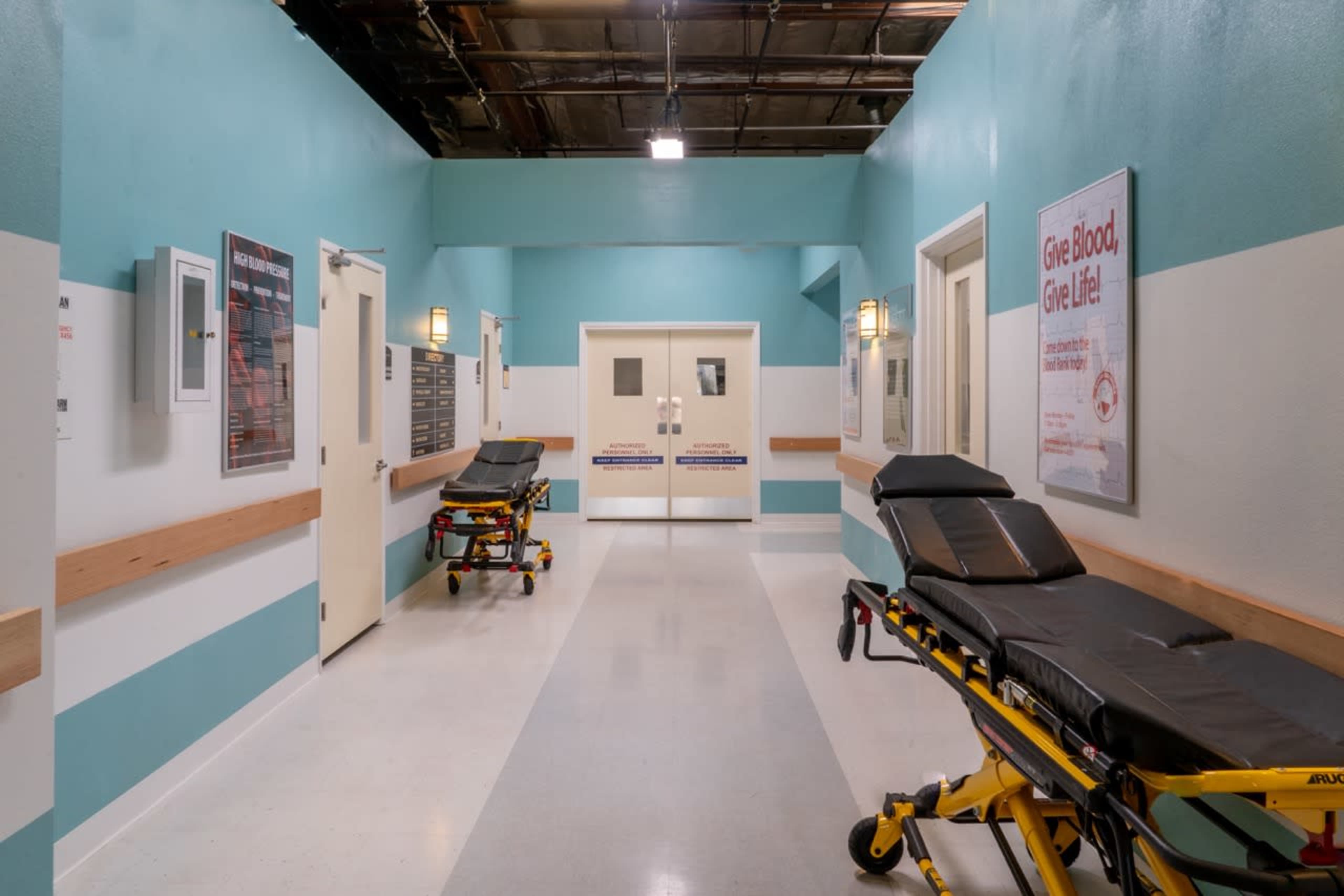A hospital corridor with two stretchers along the walls and double doors at the far end.