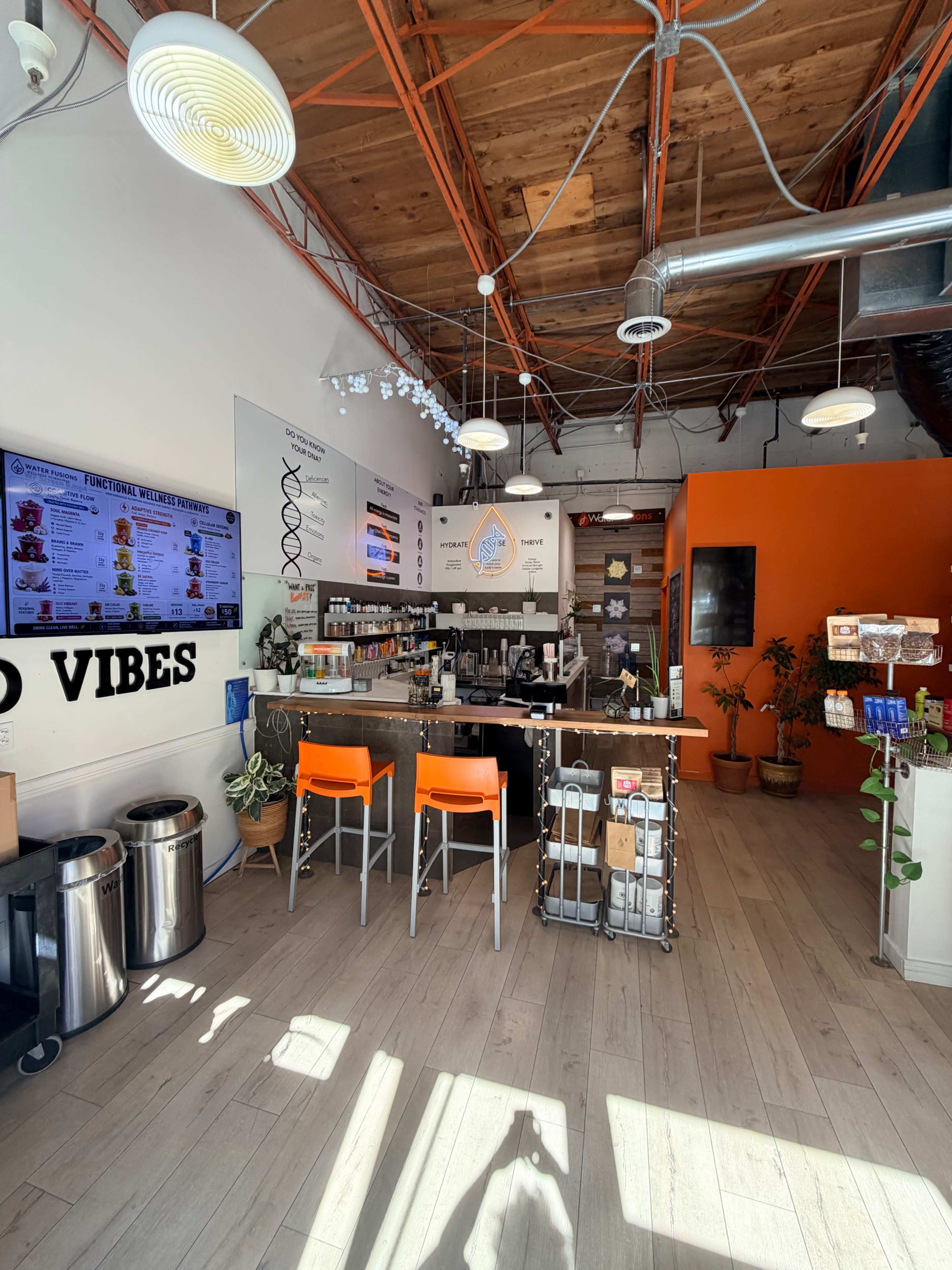 The image shows a modern café interior with orange accents, a counter filled with various food and drink items, and seating arrangements including two orange chairs.