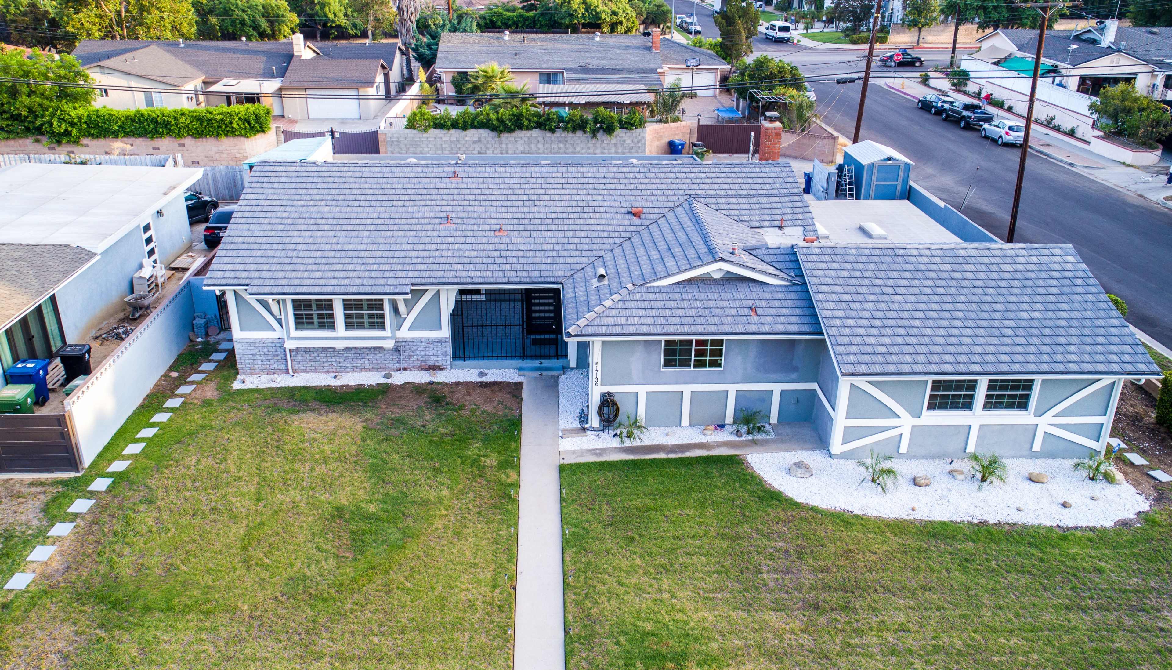 The image shows a single-story house with a gray exterior, a well-maintained front yard, and a driveway leading to the entrance.
