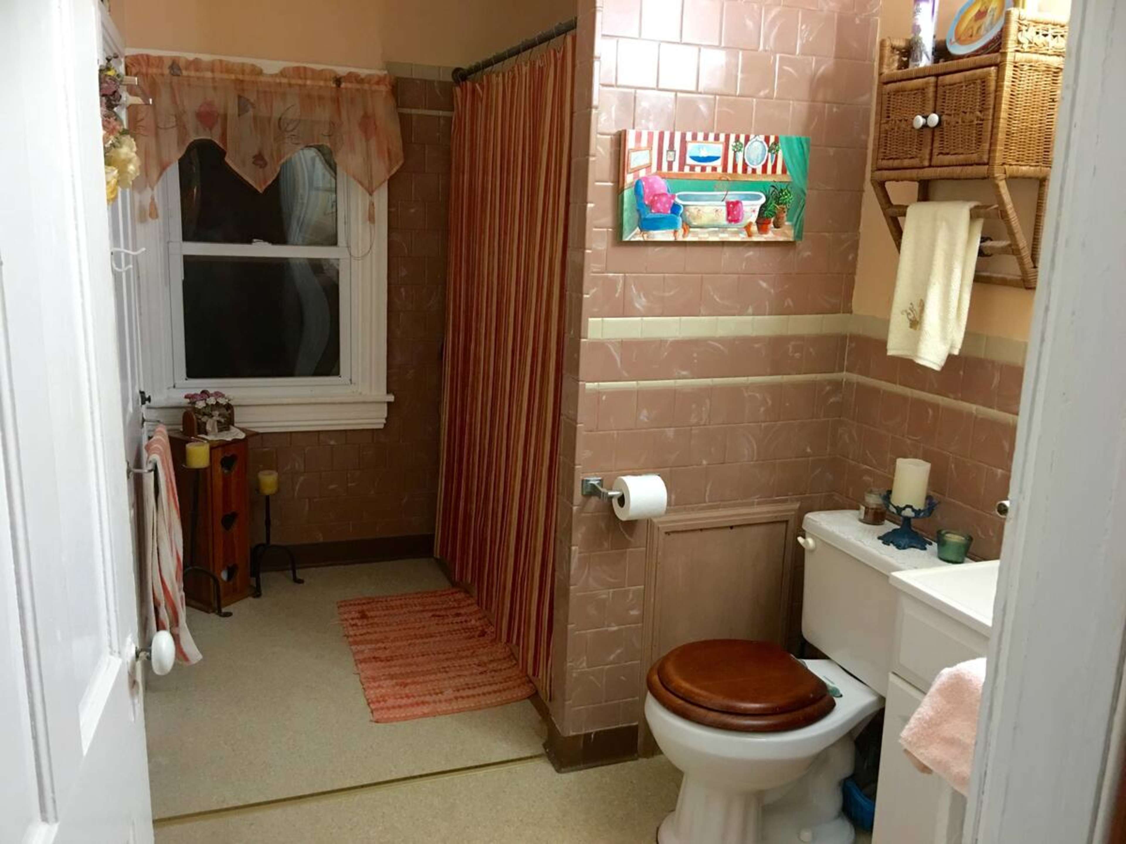 The image shows a small bathroom with beige tiled walls, a shower curtain, and a toilet next to a window.