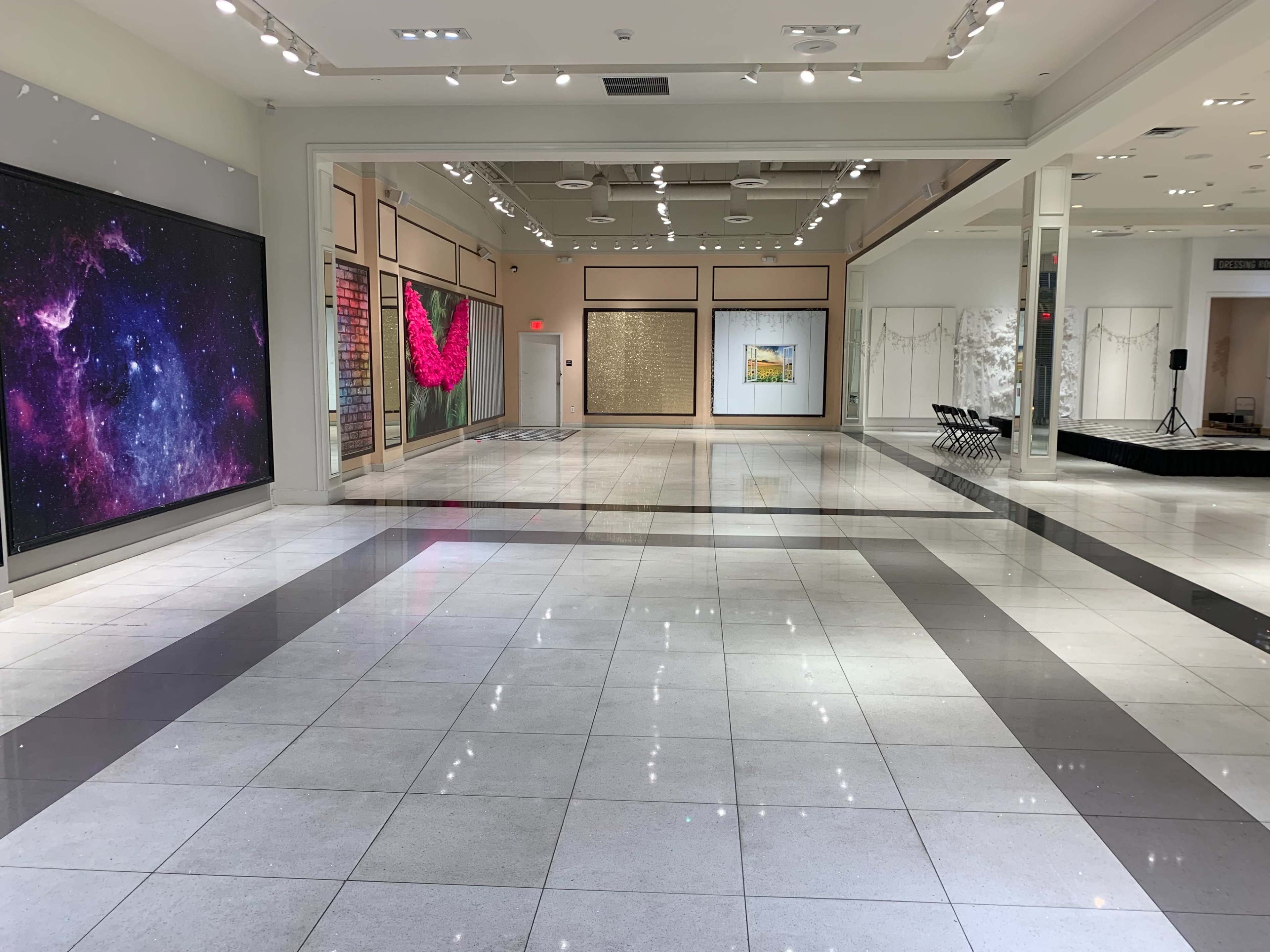 A spacious art gallery with polished tile flooring, featuring large artworks on the walls and a seating area in the background.
