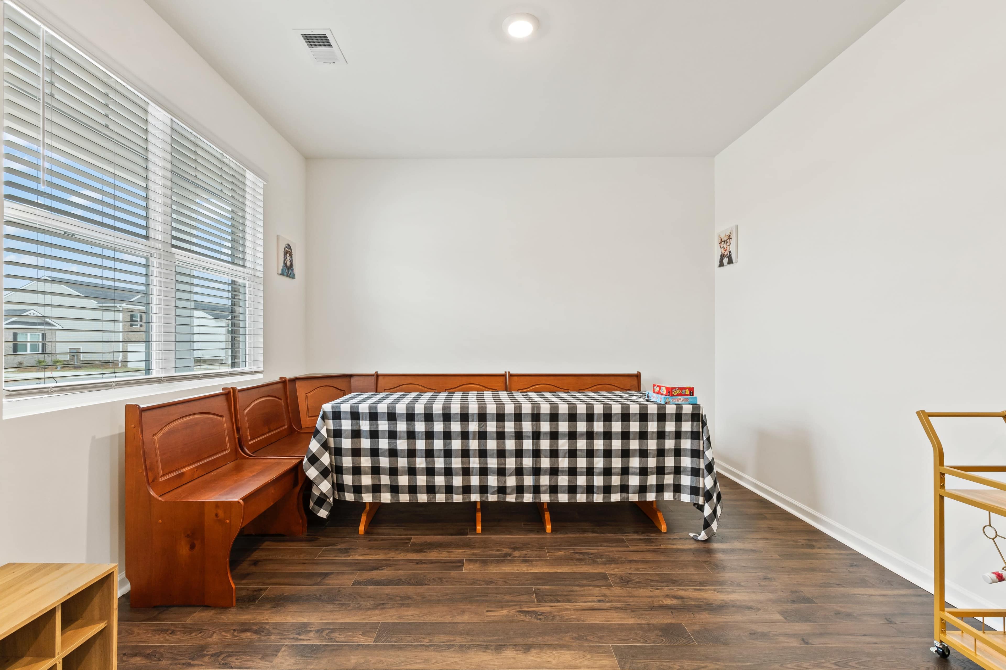 A room with a wooden bench, a table covered in a black and white checkered tablecloth, and windows allowing natural light to enter.