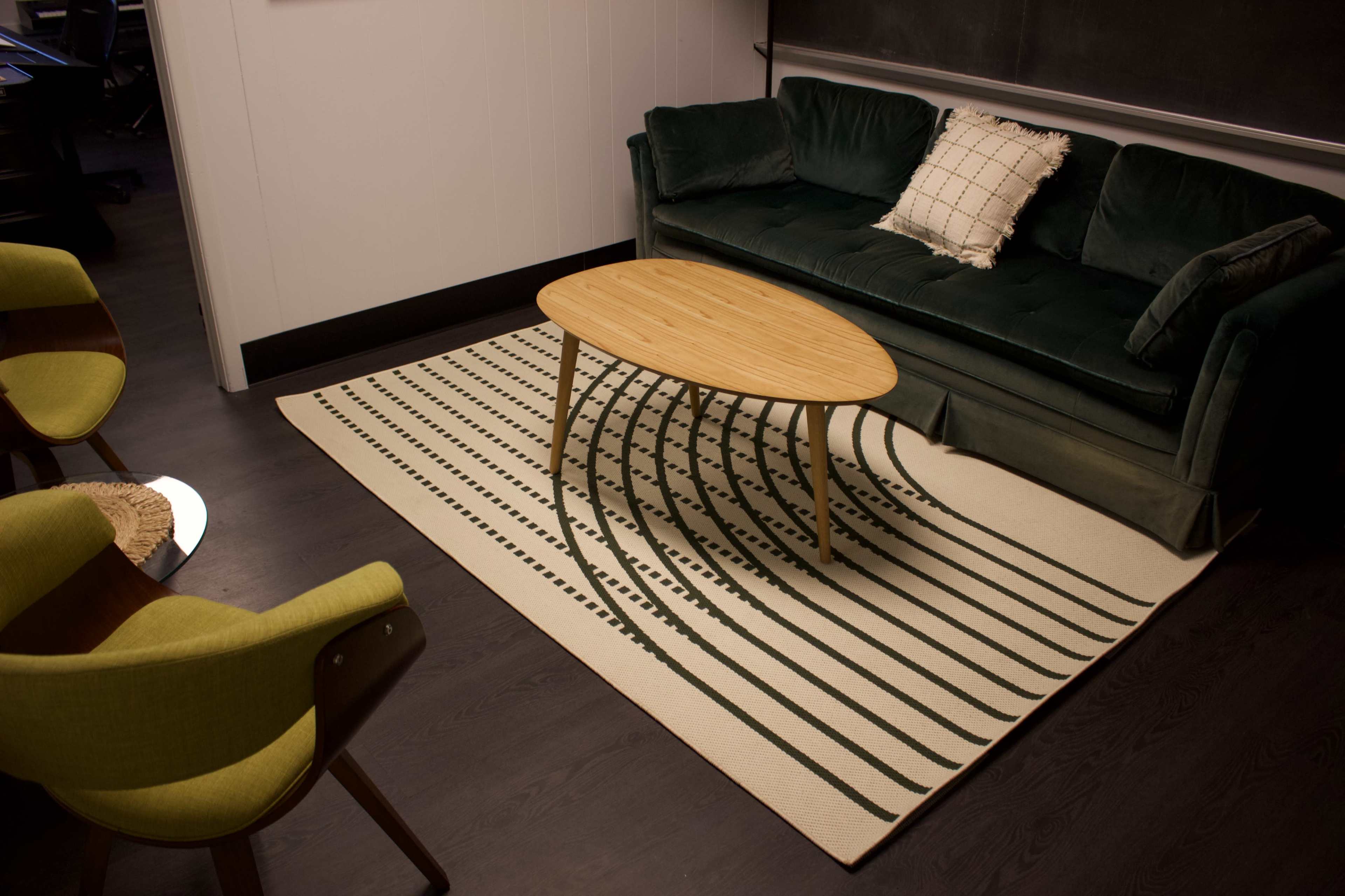 A green sofa with a pillow, a round wooden coffee table, and a patterned area rug on a dark floor in a cozy living space.