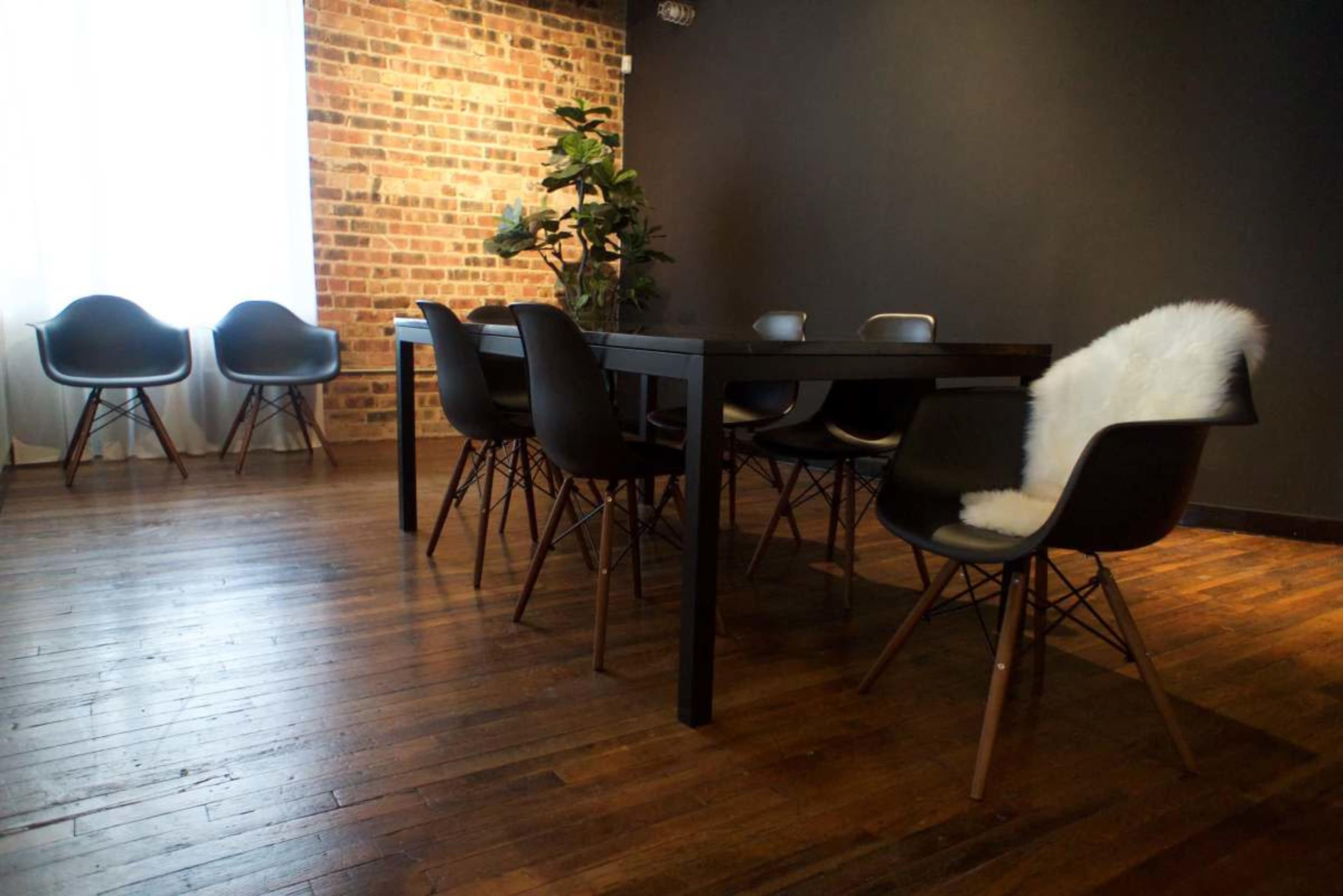 A modern dining area features a large black table surrounded by minimalist chairs, with a textured brick wall and wooden floor.