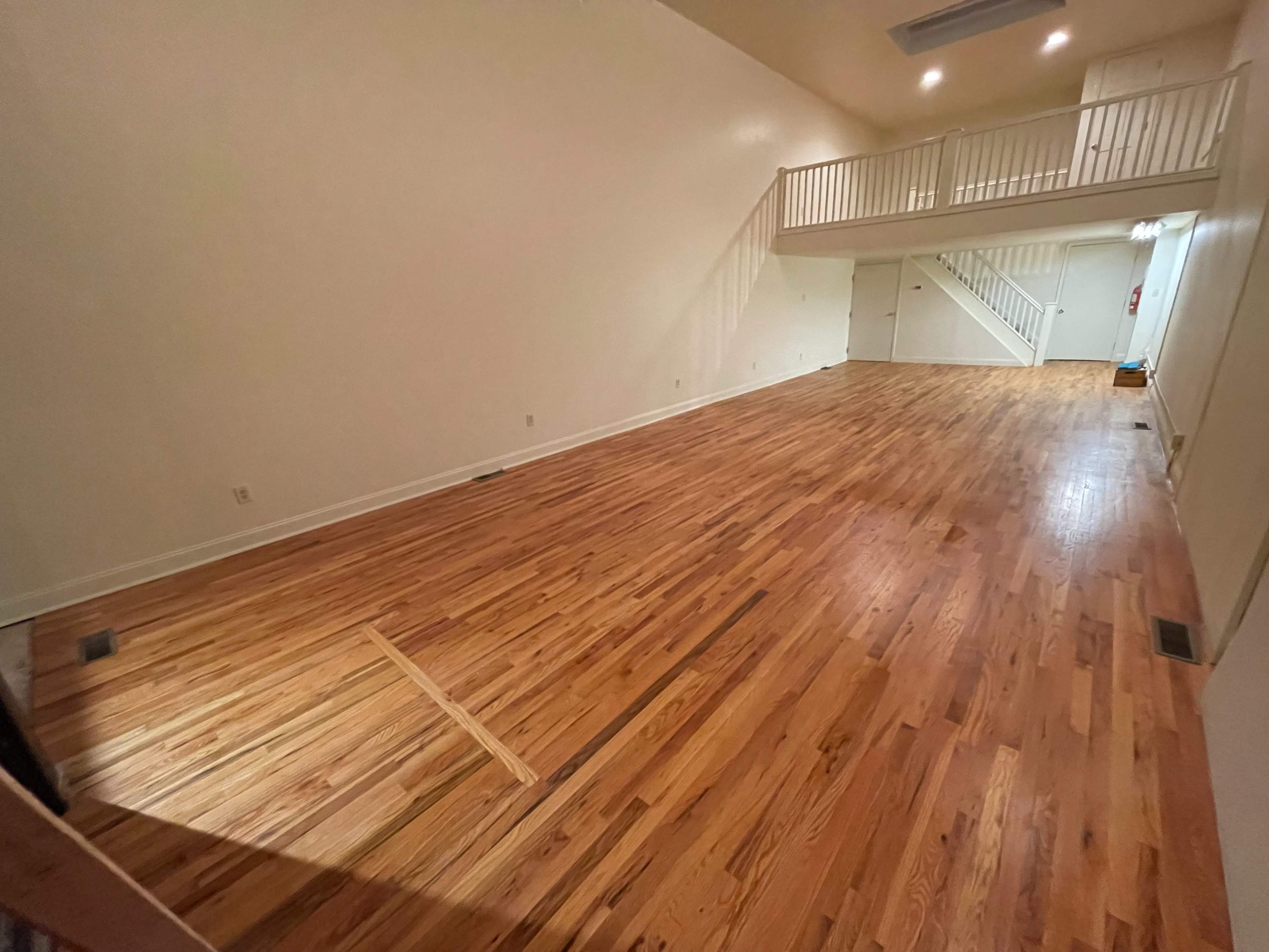 A spacious room with polished wooden floors and a staircase leading to a balcony area.