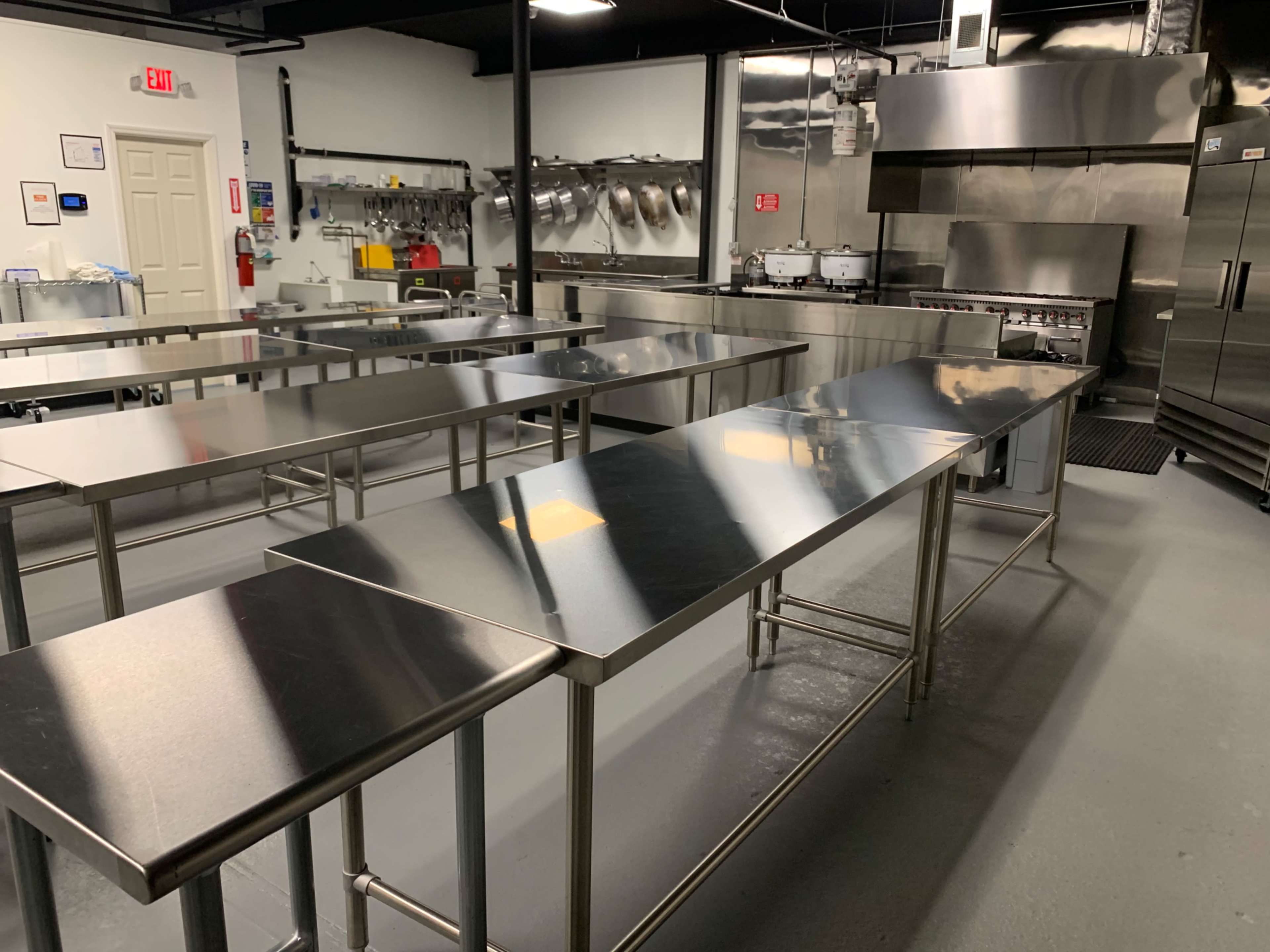 A commercial kitchen with several stainless steel tables and industrial cooking equipment.