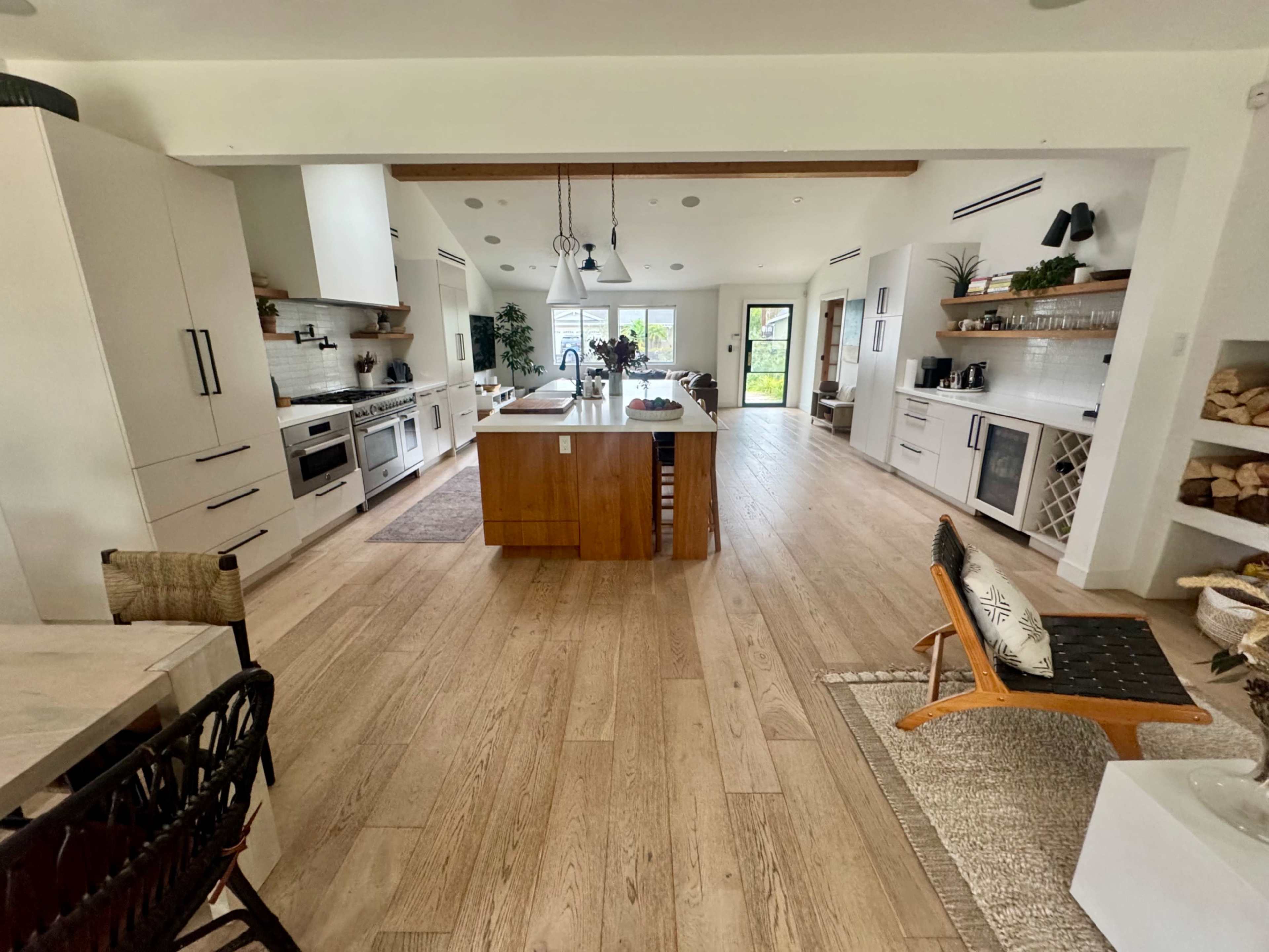 The image shows a modern open-concept kitchen and living area with light wood flooring, a central island, and various kitchen appliances.