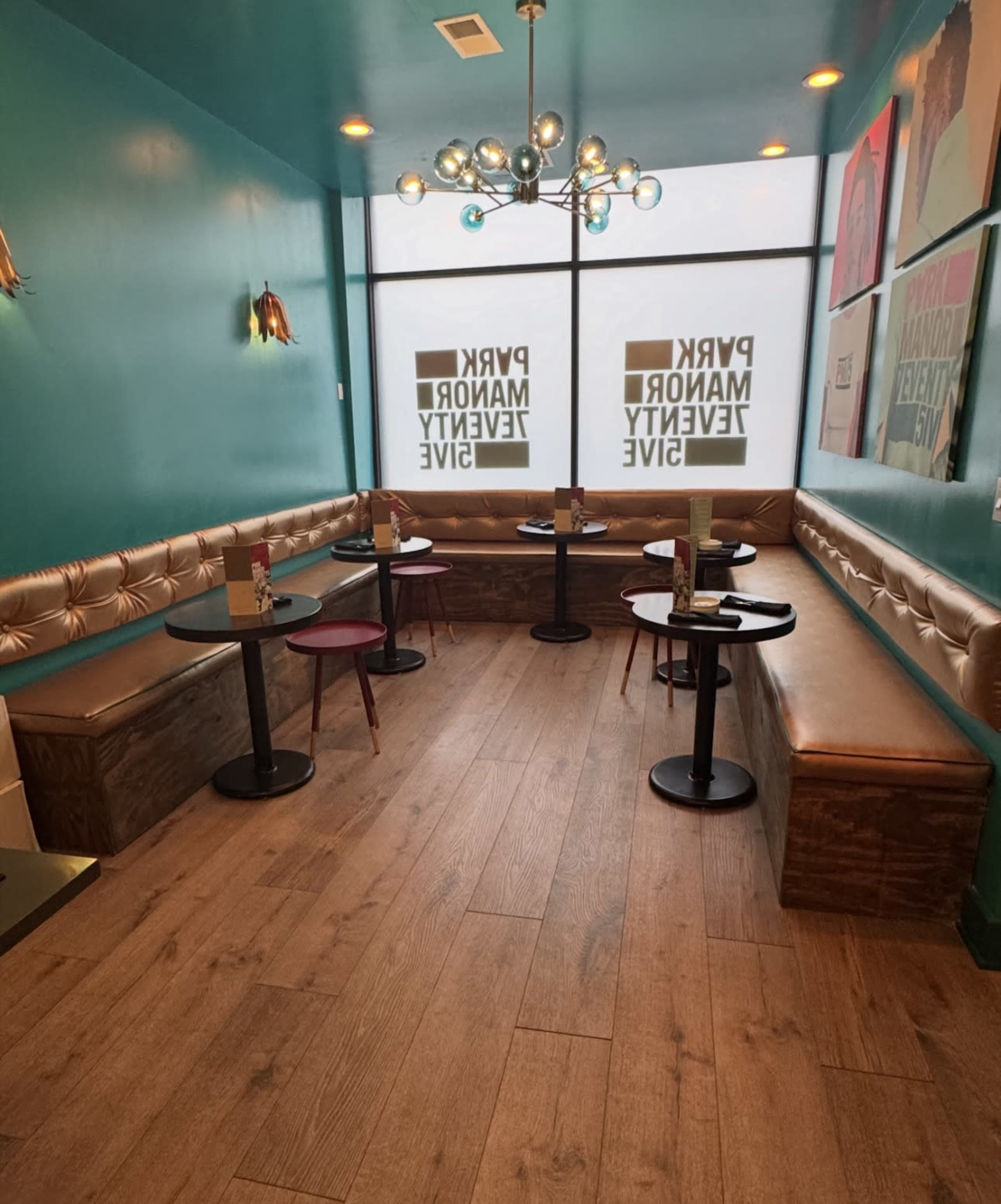 The image shows a brightly colored café interior with turquoise walls, booth seating along one side, and round tables arranged in the center.