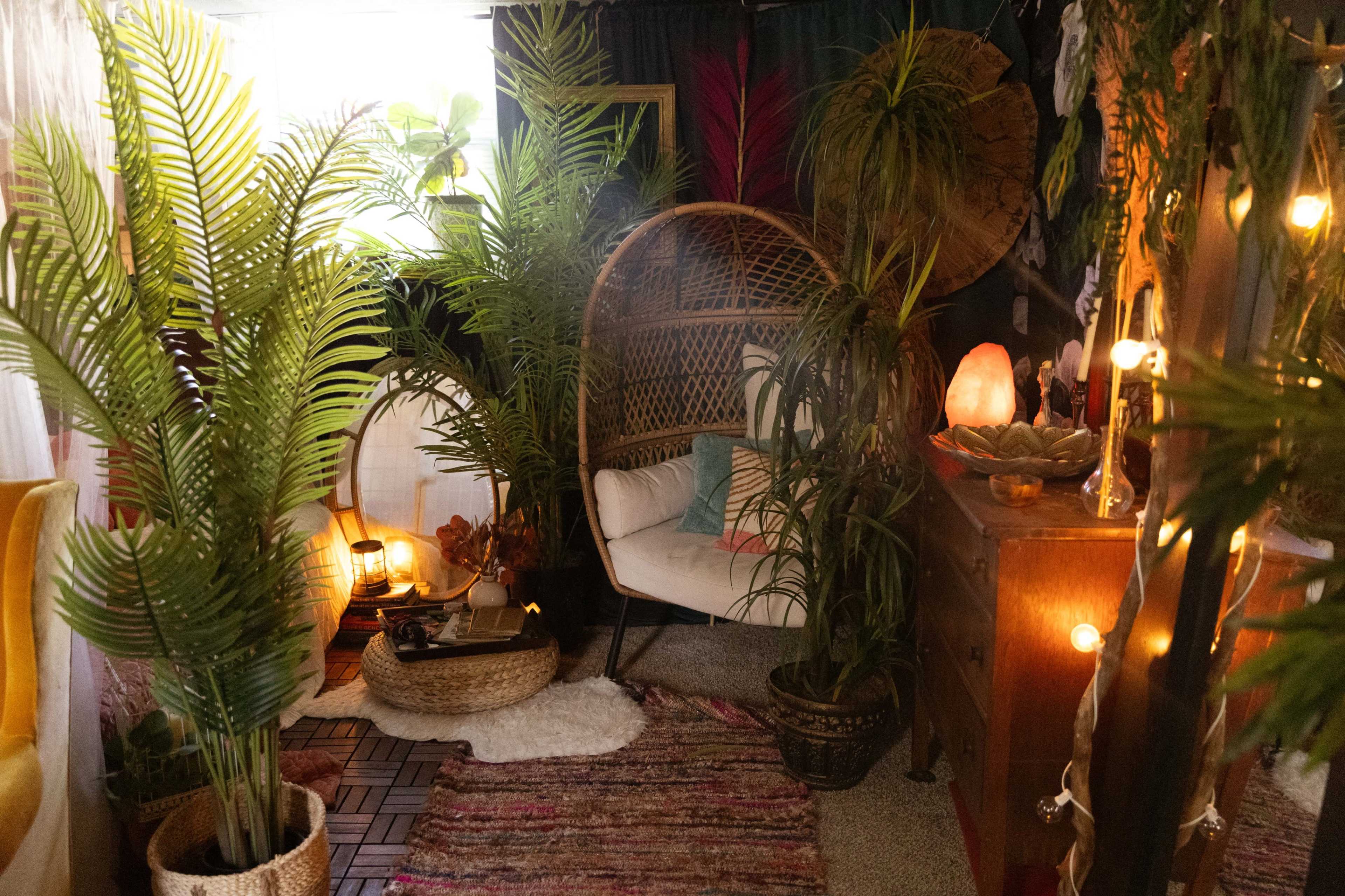 A cozy indoor space adorned with various plants, a rattan chair, a wooden dresser, and warm lighting.