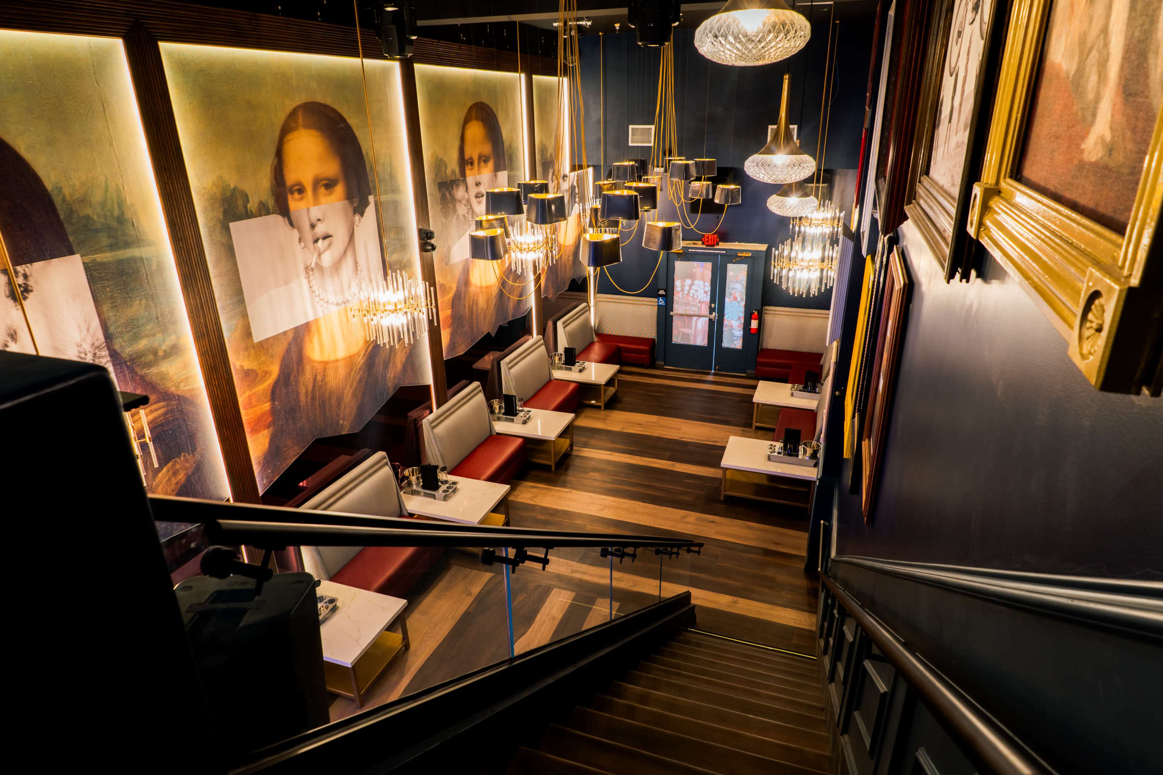 A restaurant interior featuring seating areas with white tables and red upholstered benches, highlighted by large portraits on the walls and decorative chandeliers.