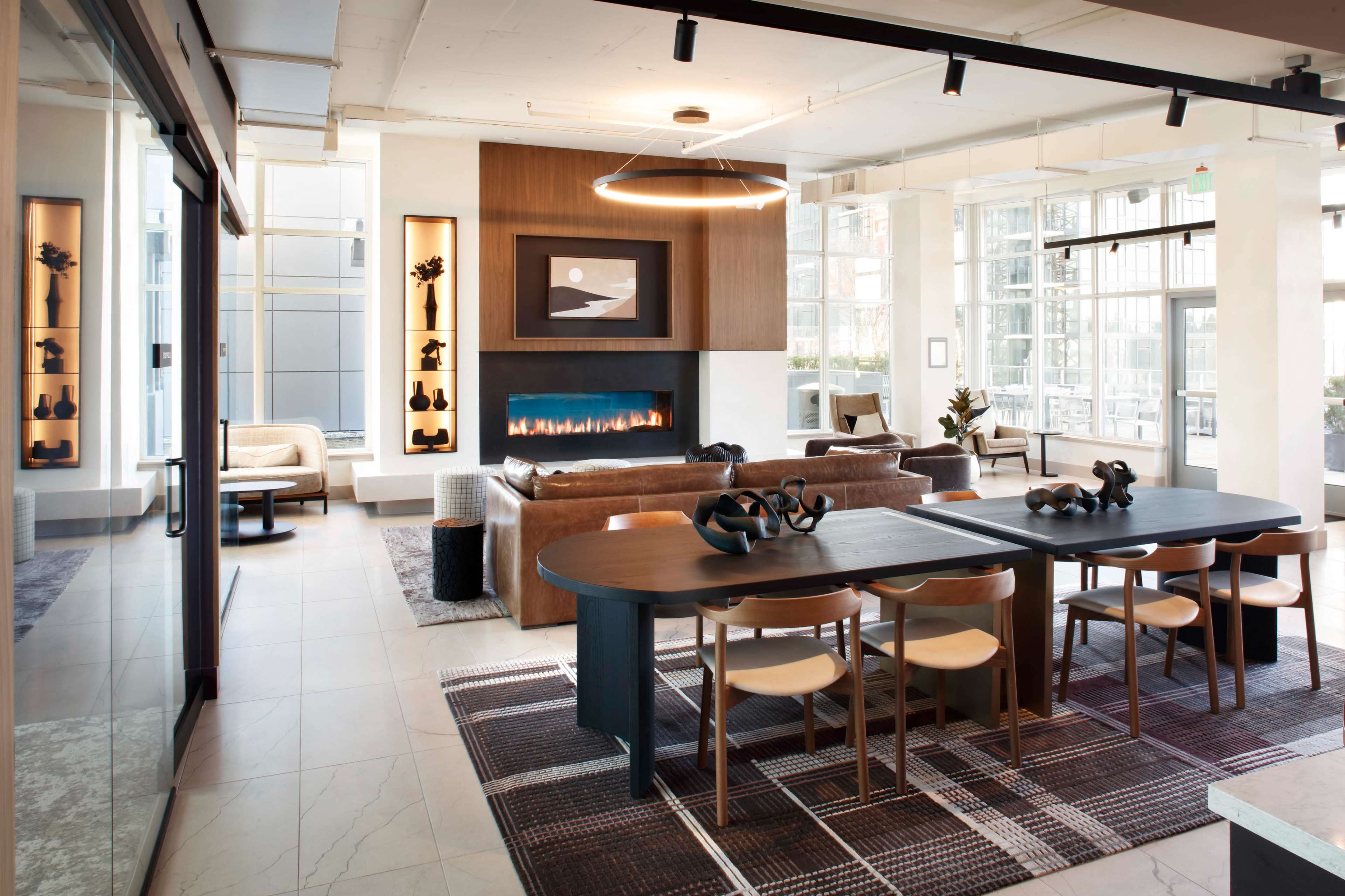 A modern, open-concept living space featuring a cozy seating area with a fireplace, a dining table, and large windows allowing natural light.