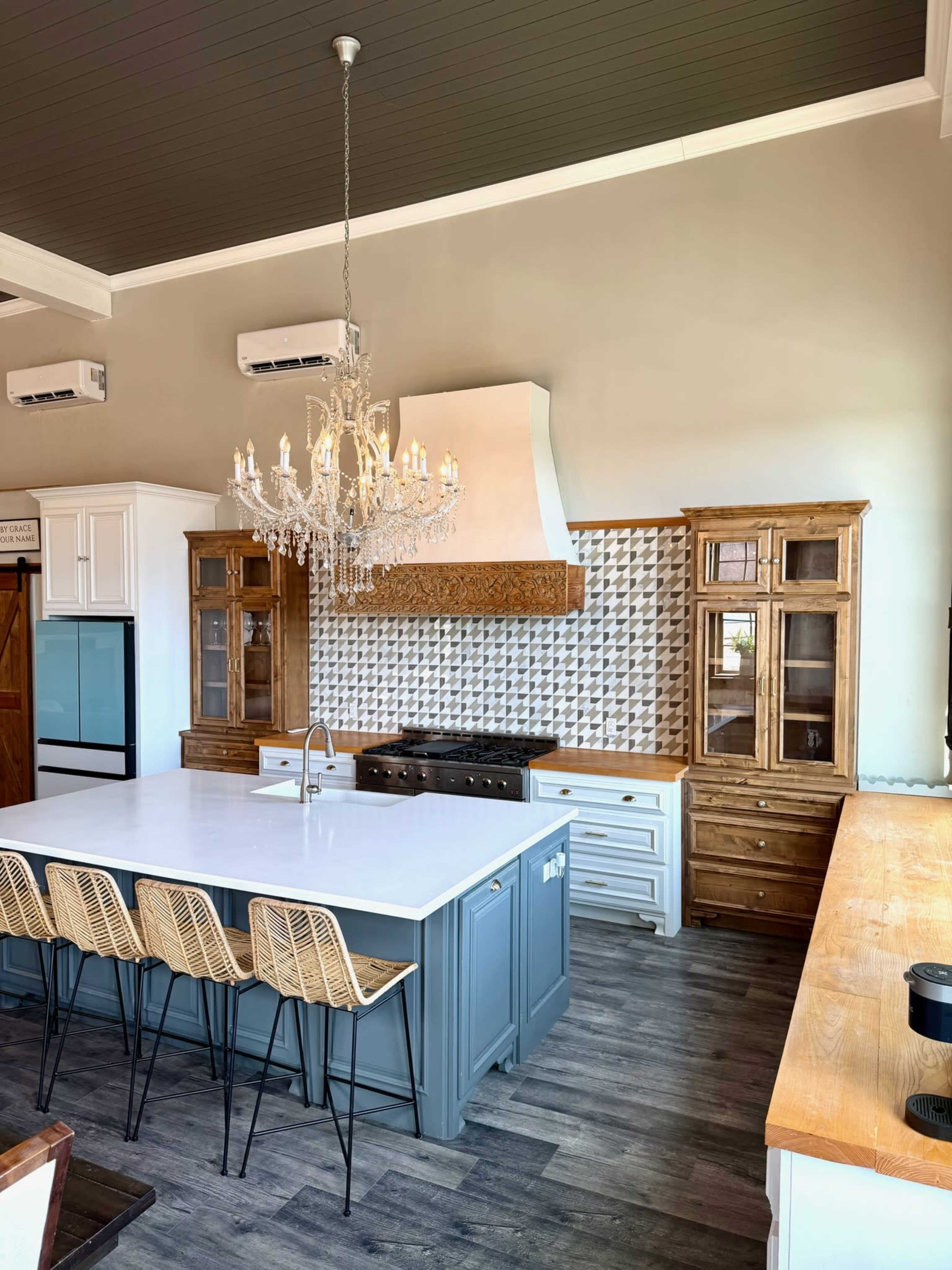 A modern kitchen features a central island with seating, a chandelier overhead, and a backsplash with a geometric design.