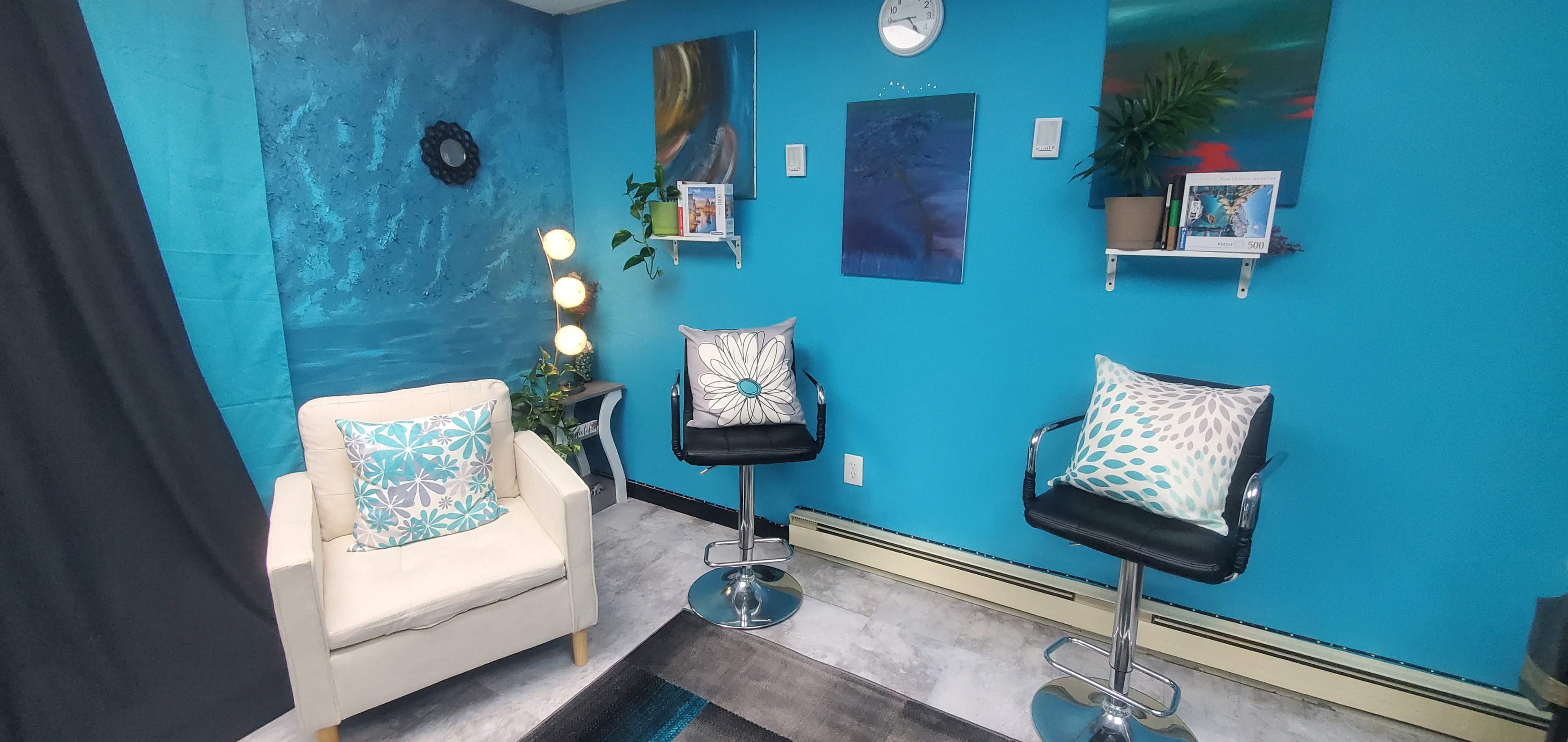 A brightly colored room with turquoise walls, featuring two decorative chairs, a small table, artwork on the walls, and a clock.