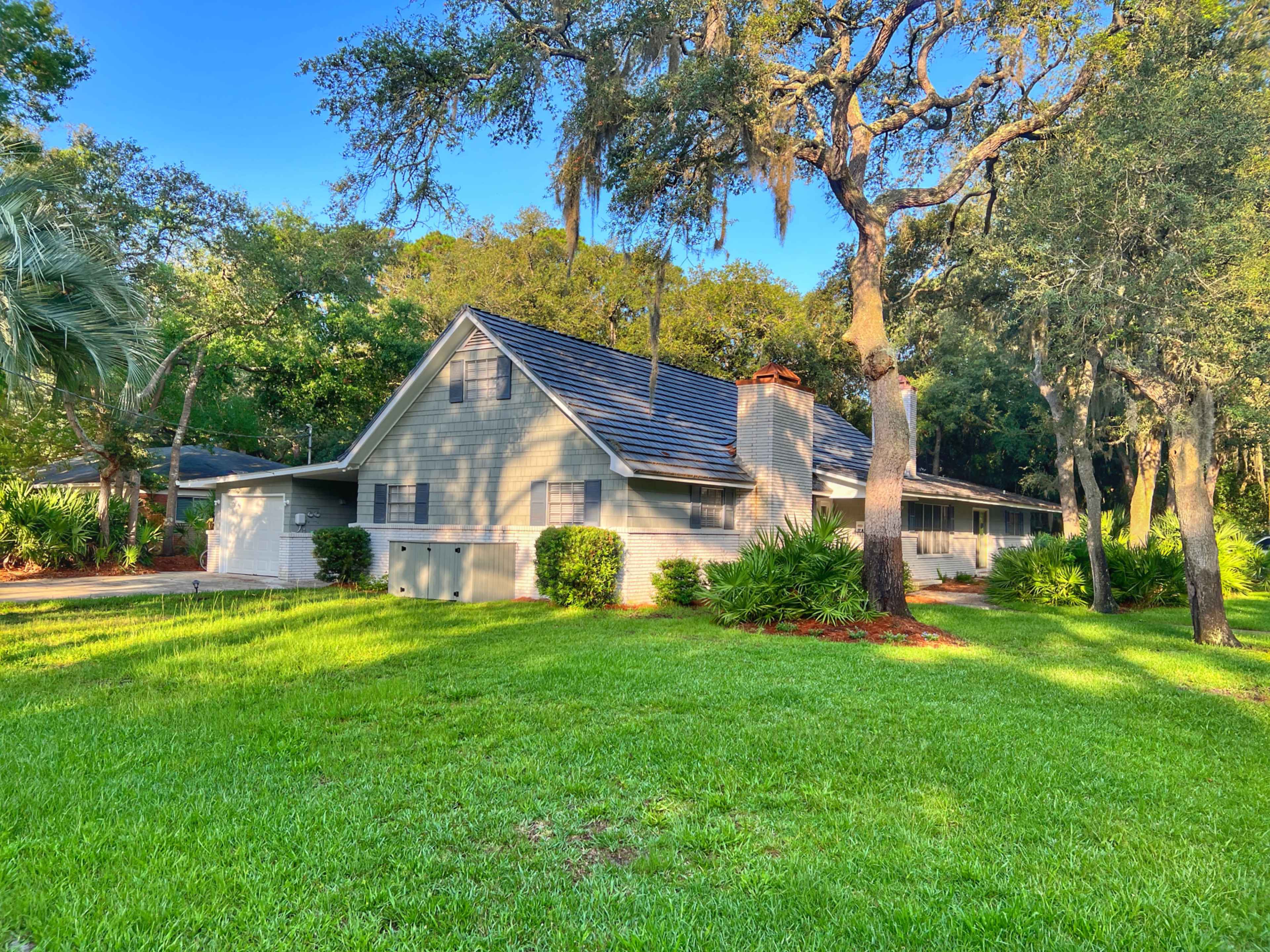 A large, two-story house with a slate roof is situated on a grassy lawn surrounded by trees.