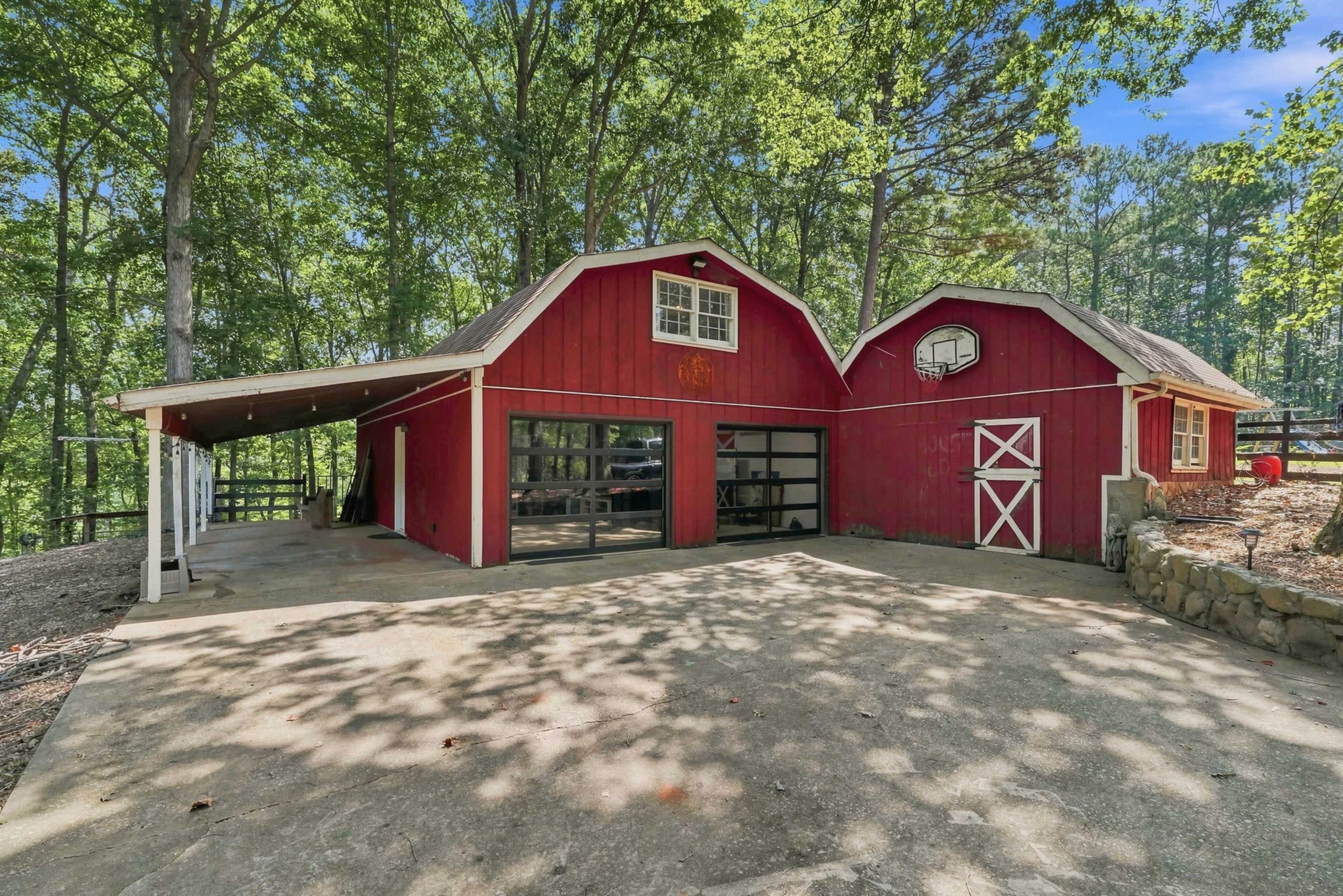 The image shows a red barn-style building with a large glass door, surrounded by trees and a concrete driveway.