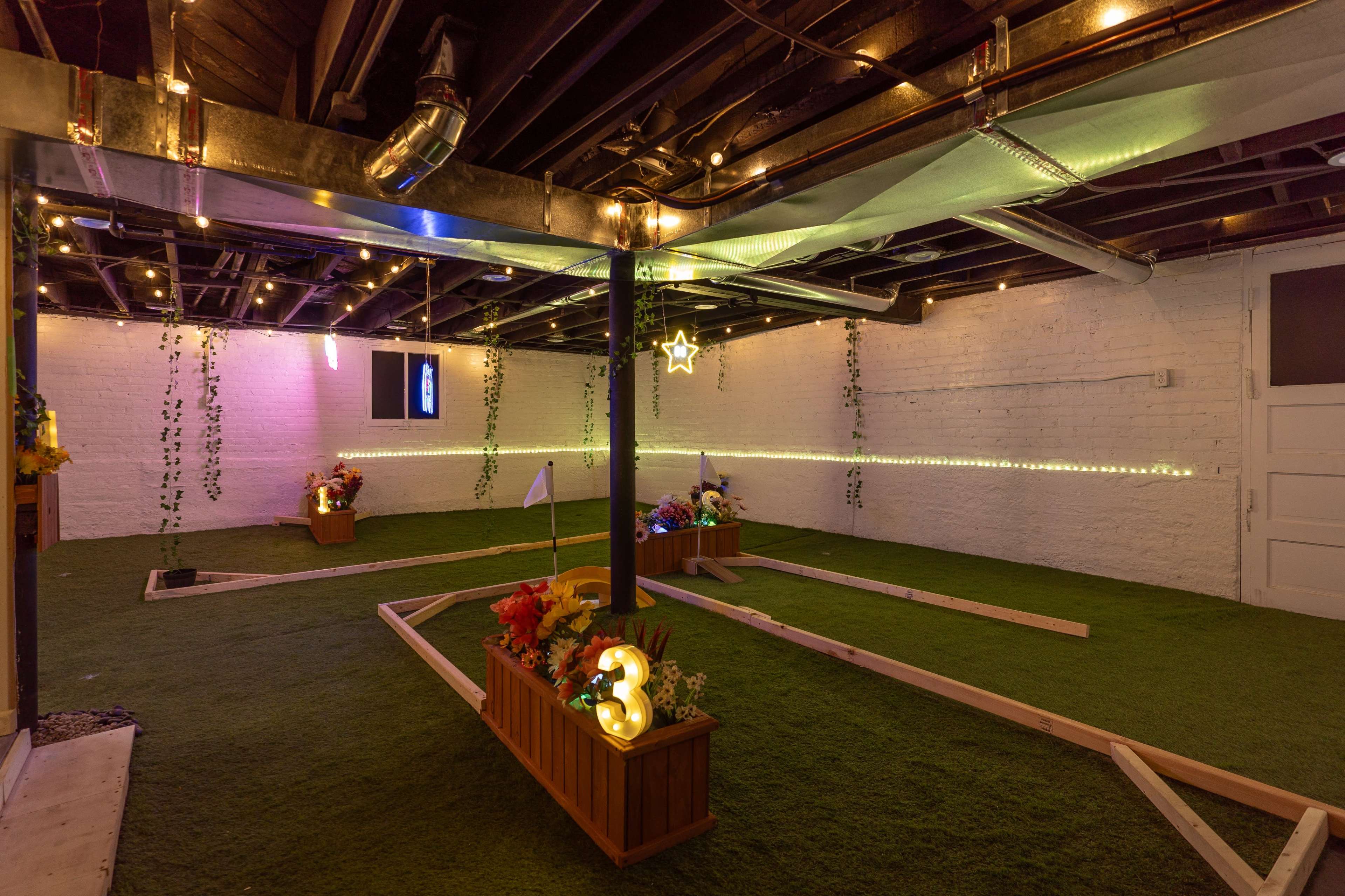 A brightly lit indoor mini-golf area with artificial grass, wooden borders, and decorative plants.