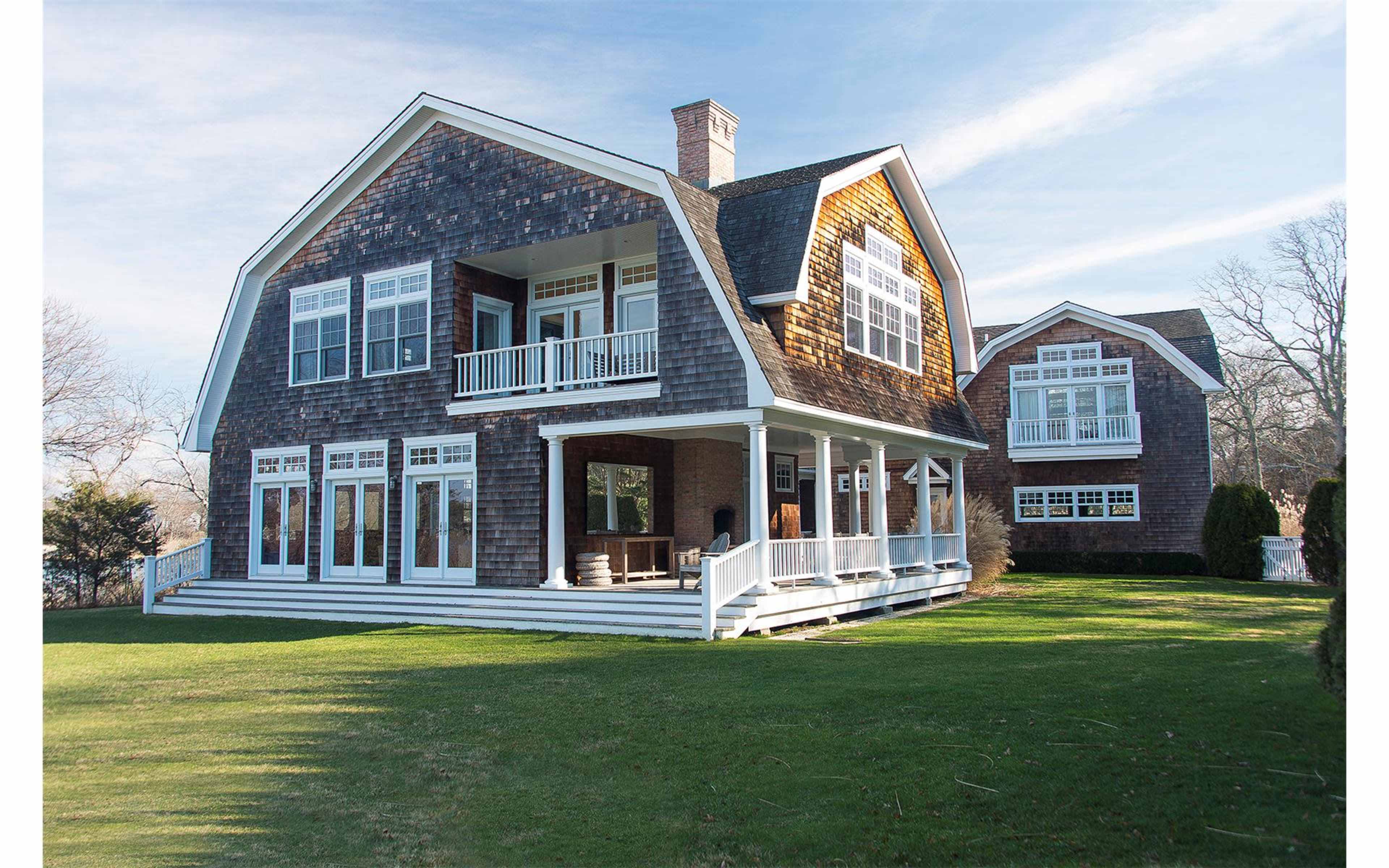 A large shingle-style house with multiple windows, a wraparound porch, and landscaped green lawns.