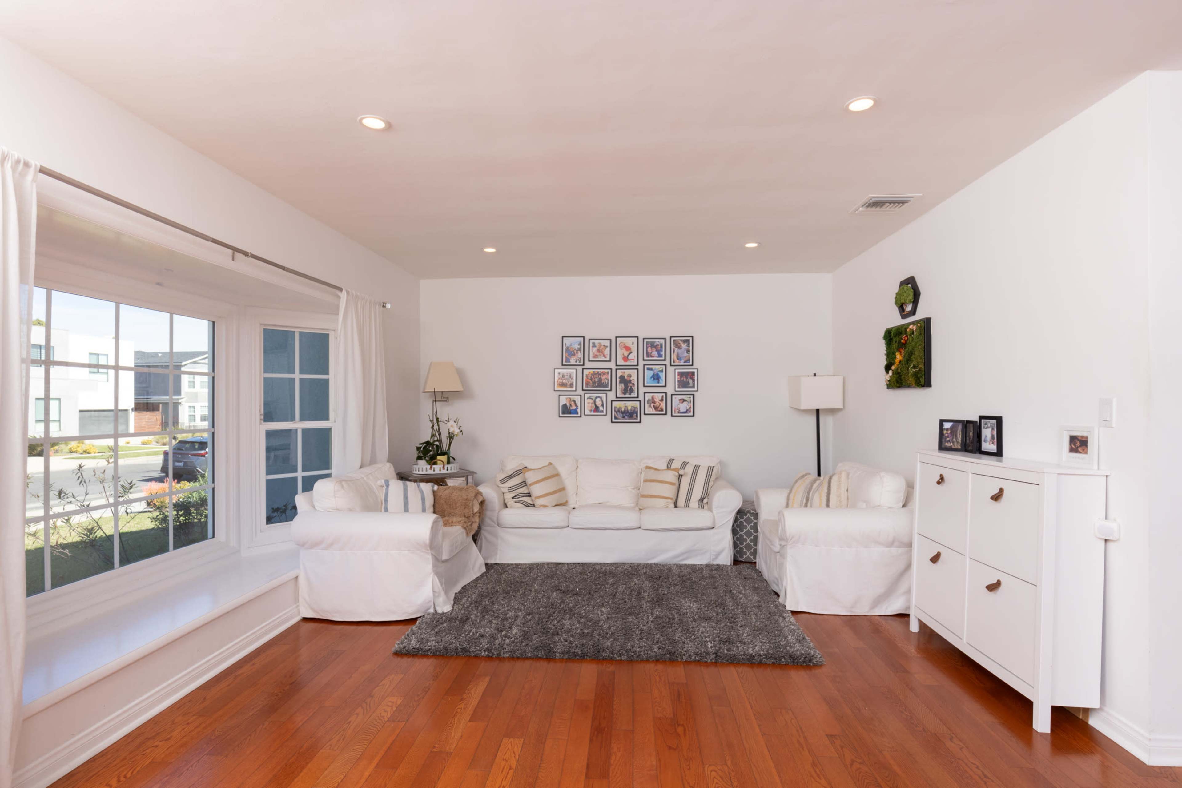 The image features a living room with white couches, a gray rug, and a gallery wall of photos above a white cabinet.