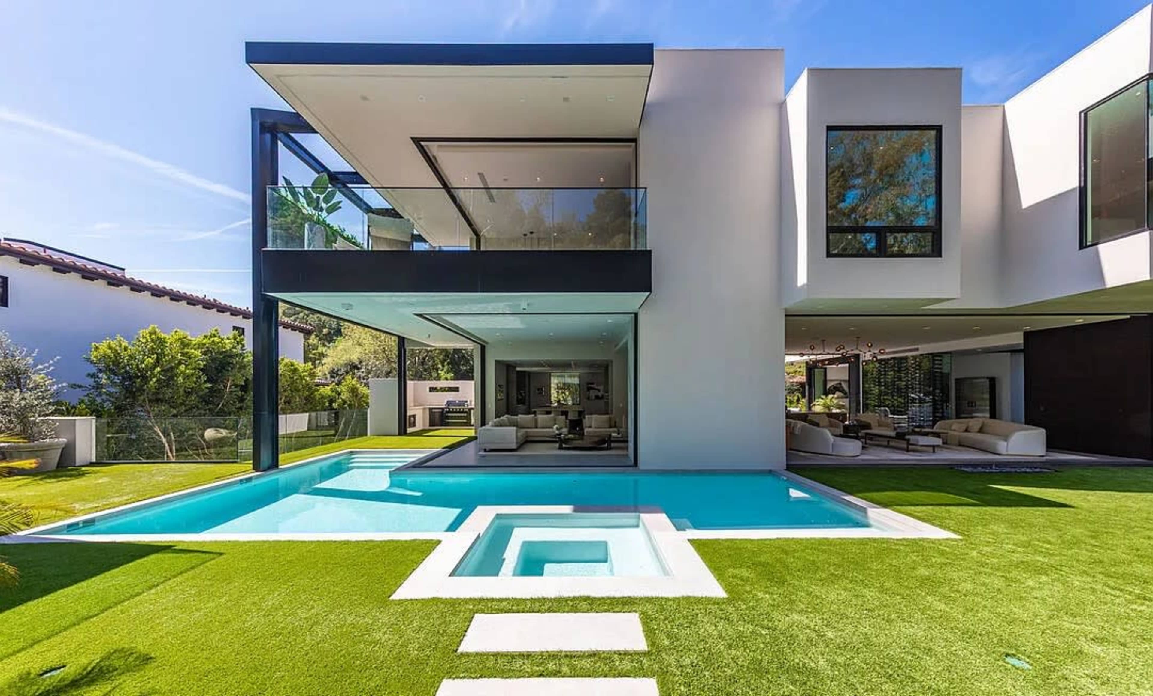 The image shows a modern two-story house with large windows, a swimming pool in the foreground, and a well-manicured lawn.