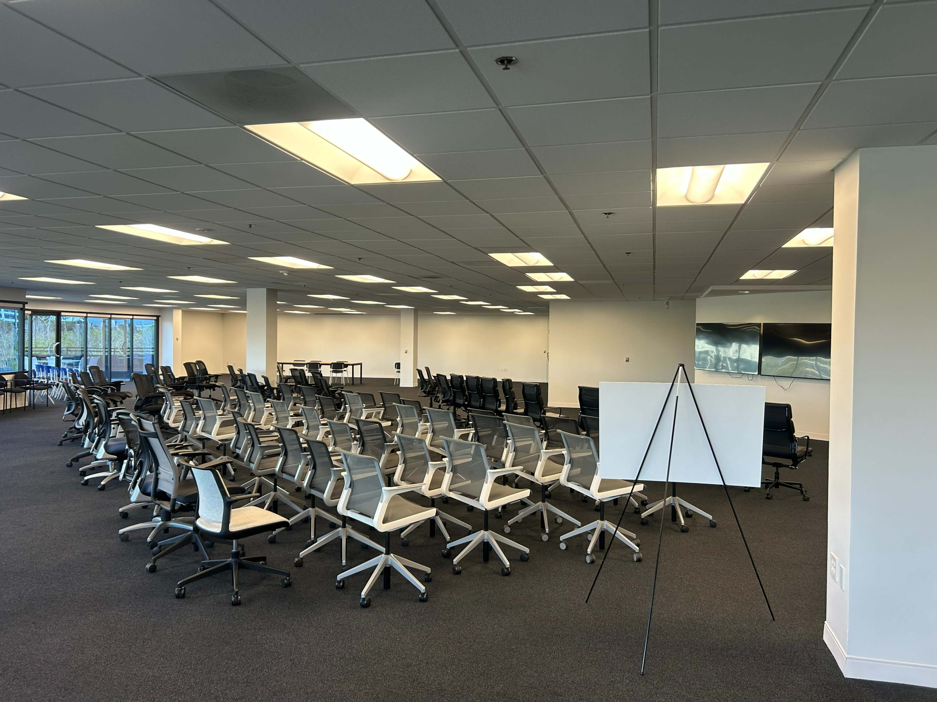 The image shows a spacious office area arranged with rows of chairs and a large blank whiteboard on an easel.