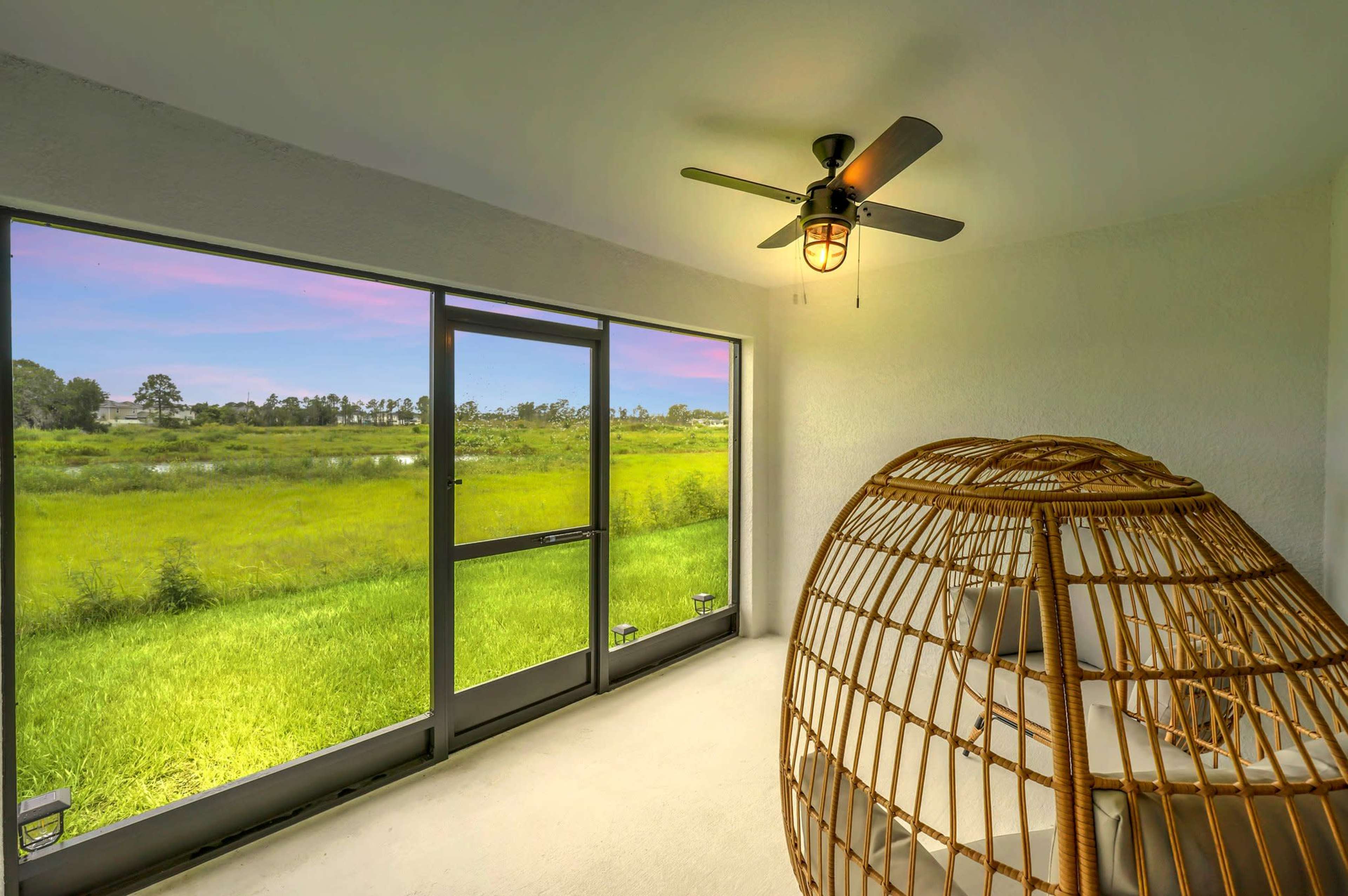 A spacious room features a large window view of a grassy landscape and a unique wicker hanging chair.