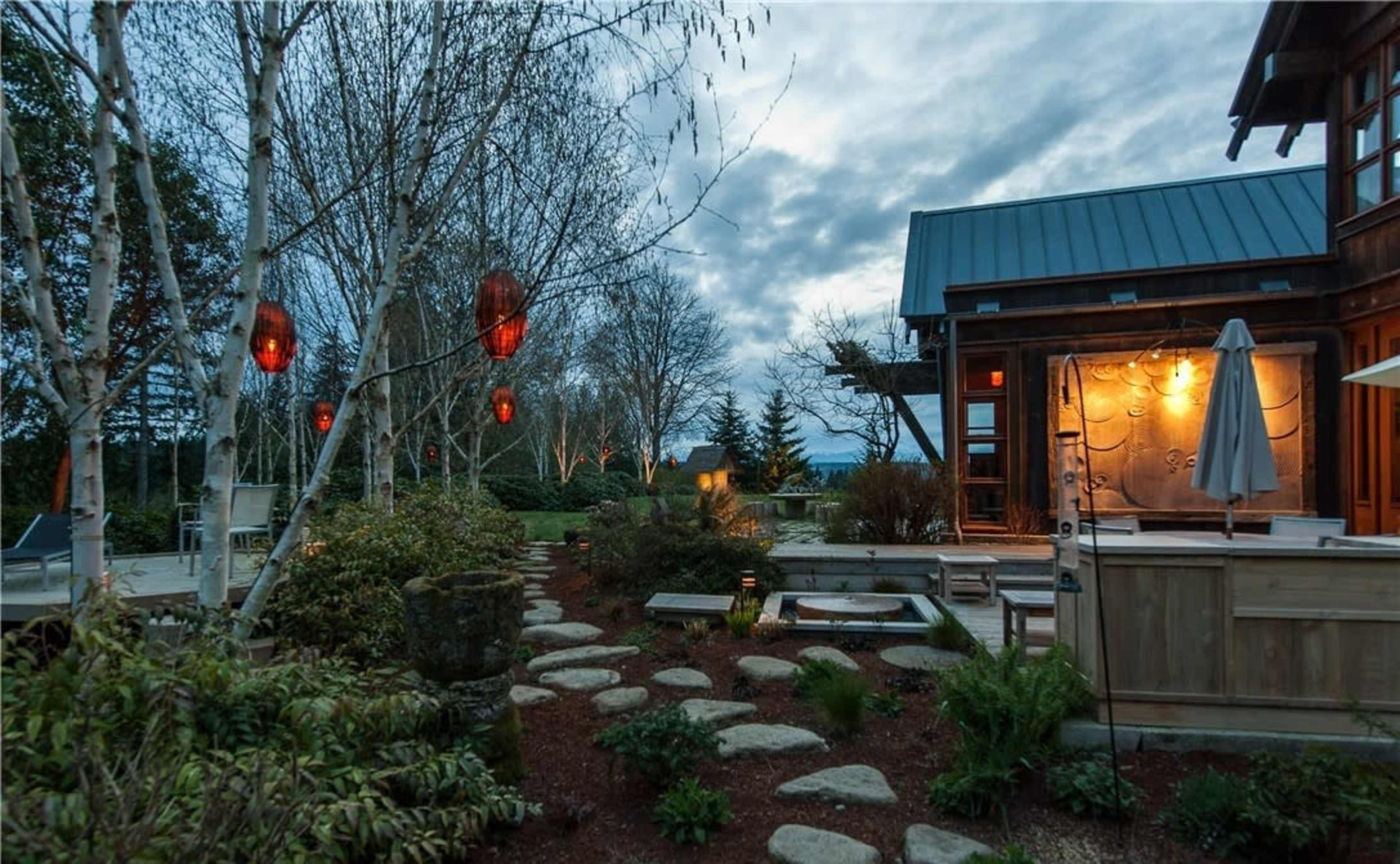 The scene features a landscaped garden with stone pathways leading to a wooden structure under a cloudy sky, illuminated by red lanterns.