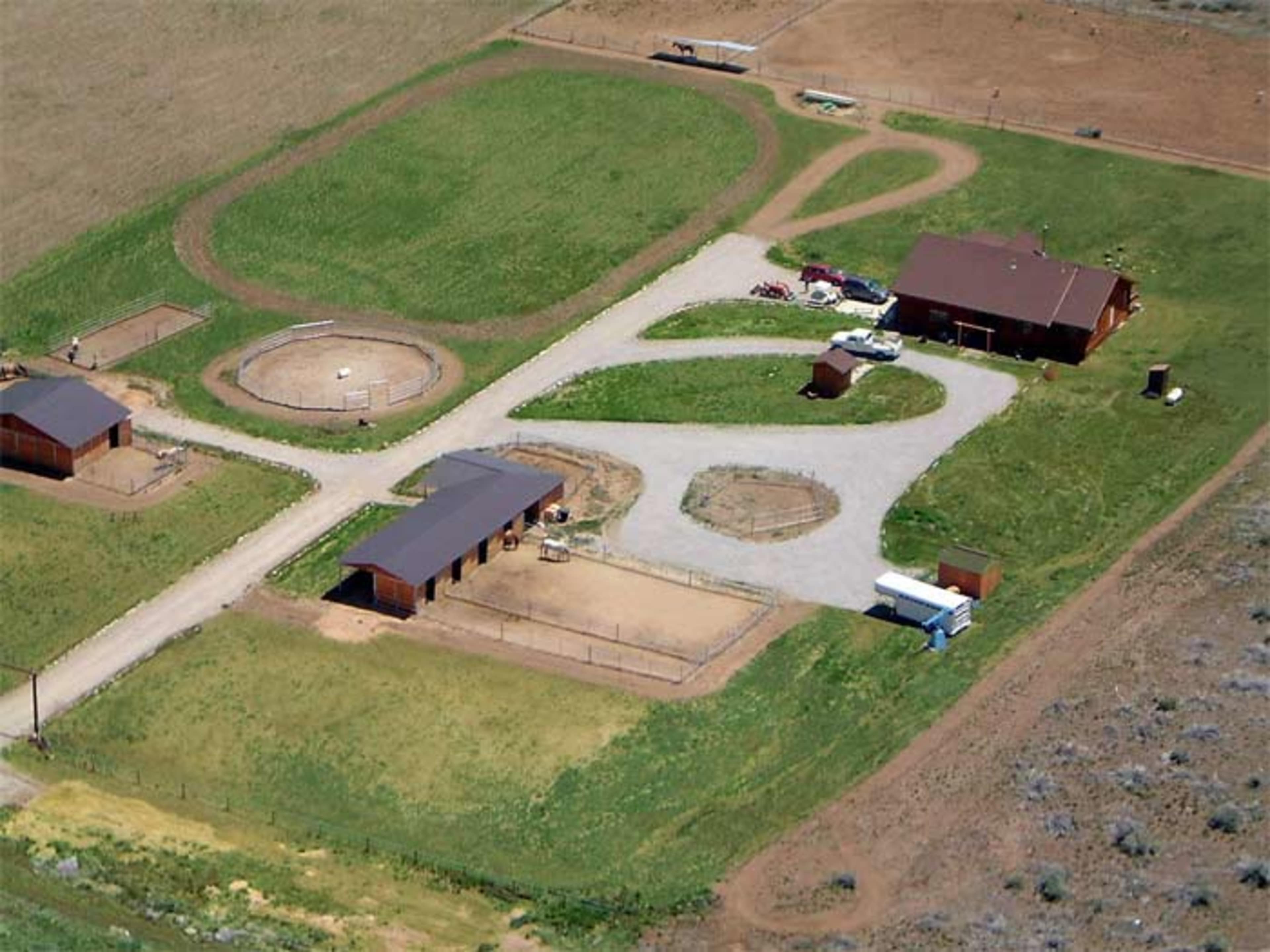 An aerial view of a ranch with multiple buildings, fenced enclosures, and grassy areas.