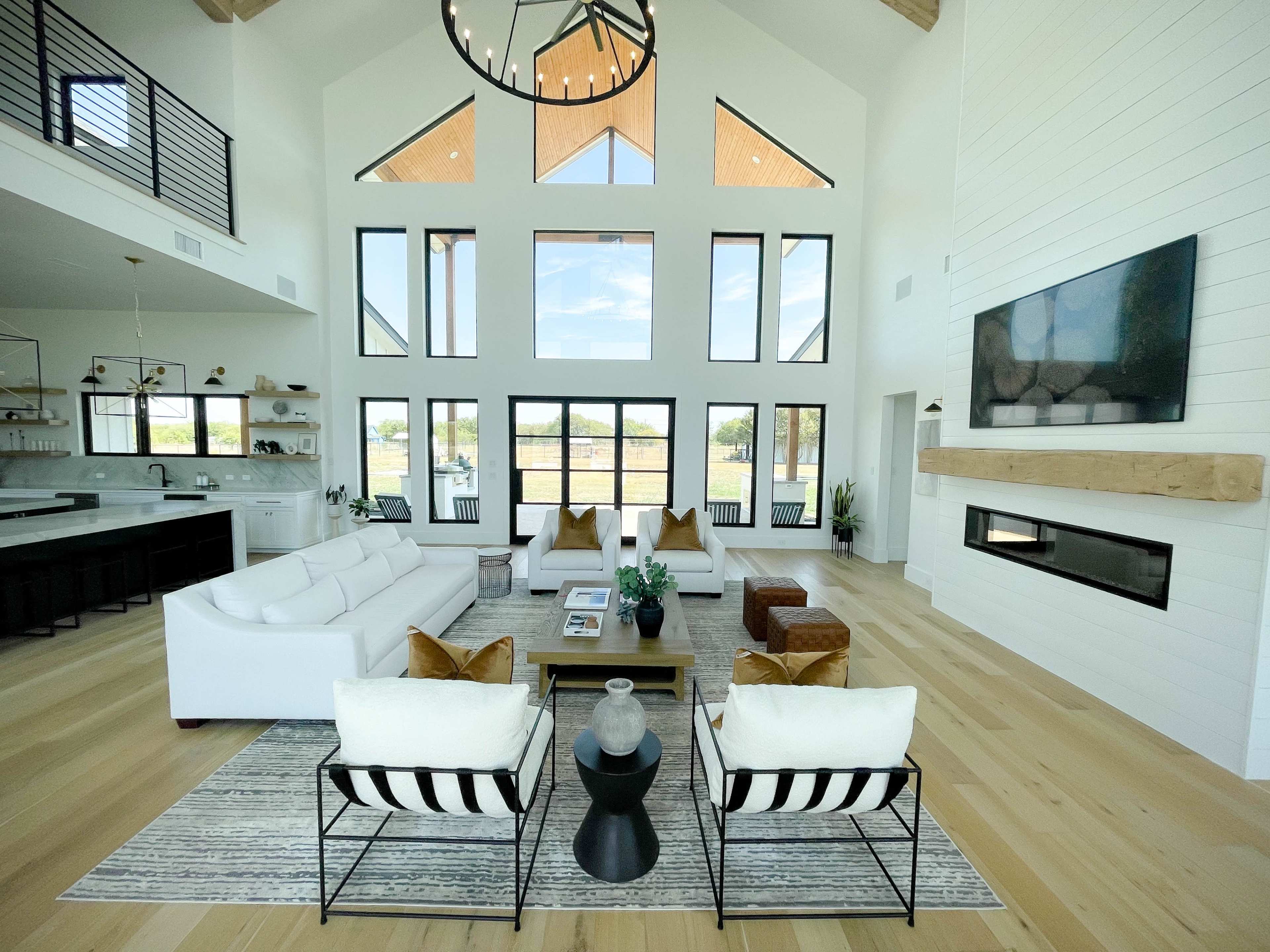 A spacious, bright living room features large windows, modern furniture, and a focal fireplace with a mounted television.