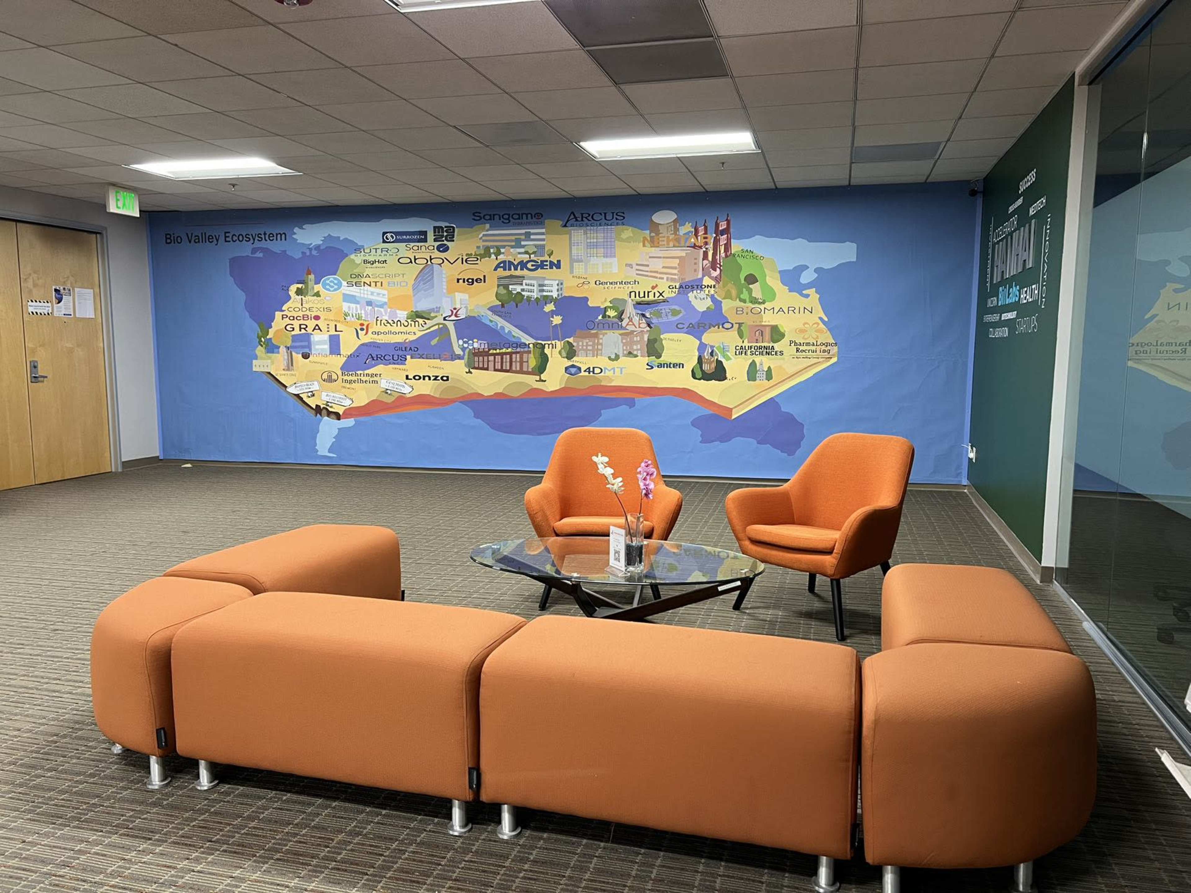 An office lounge area with orange chairs and a sectional couch in front of a large map mural of Canada.