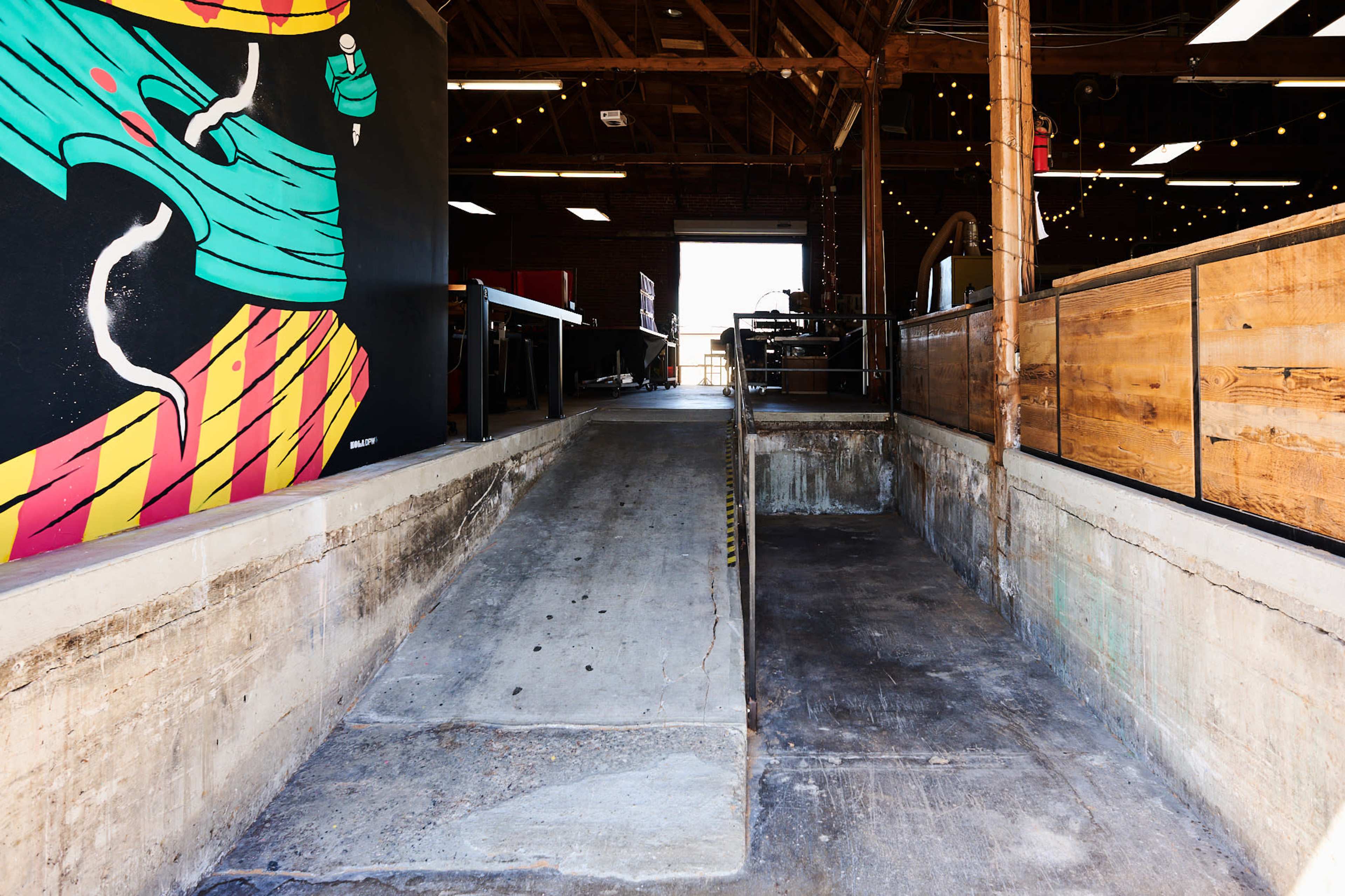 A concrete ramp leading into a well-lit industrial space with wooden structures and colorful wall art.