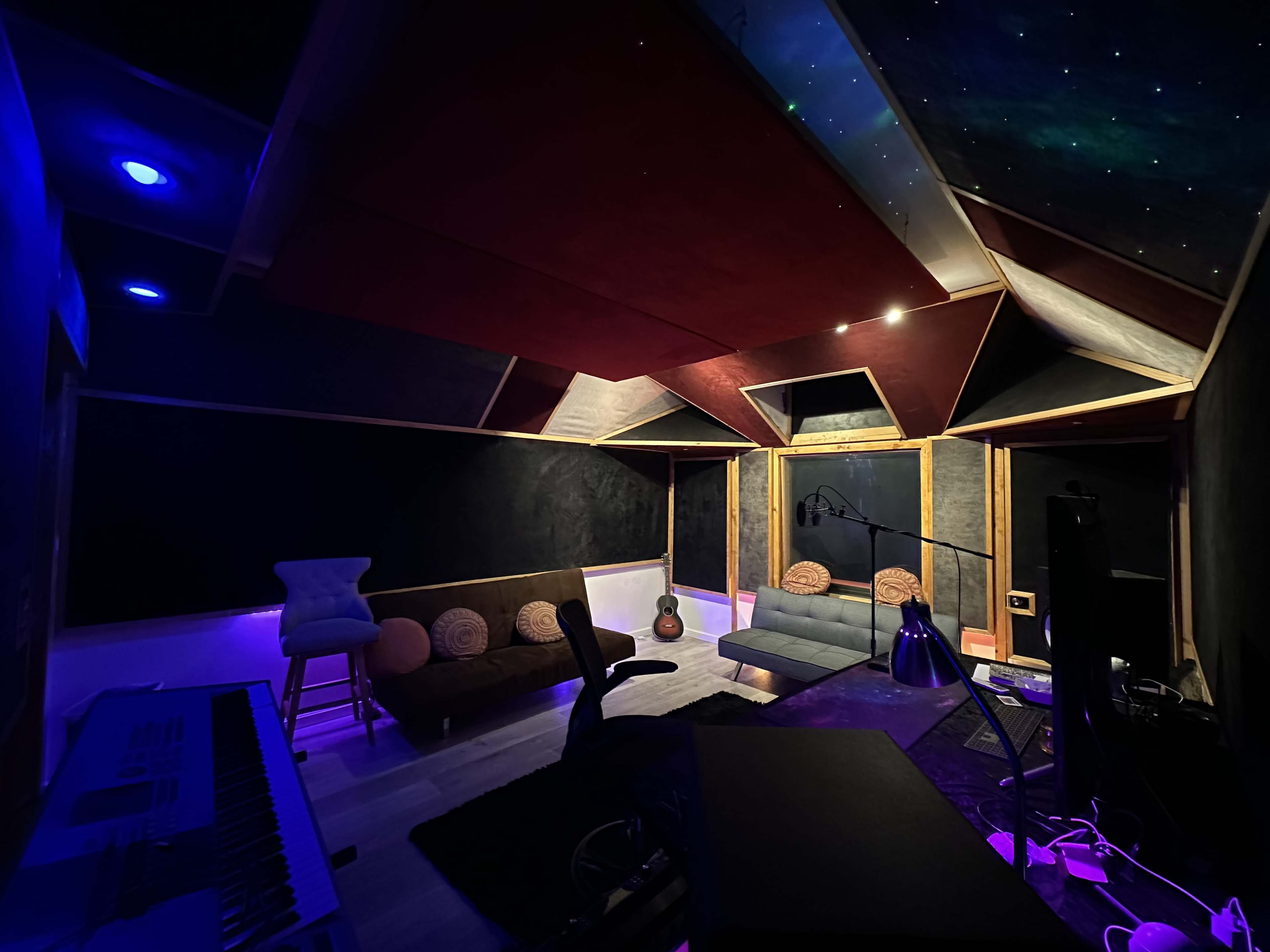 A music studio with modern furniture, acoustic panels, and colorful ambient lighting.