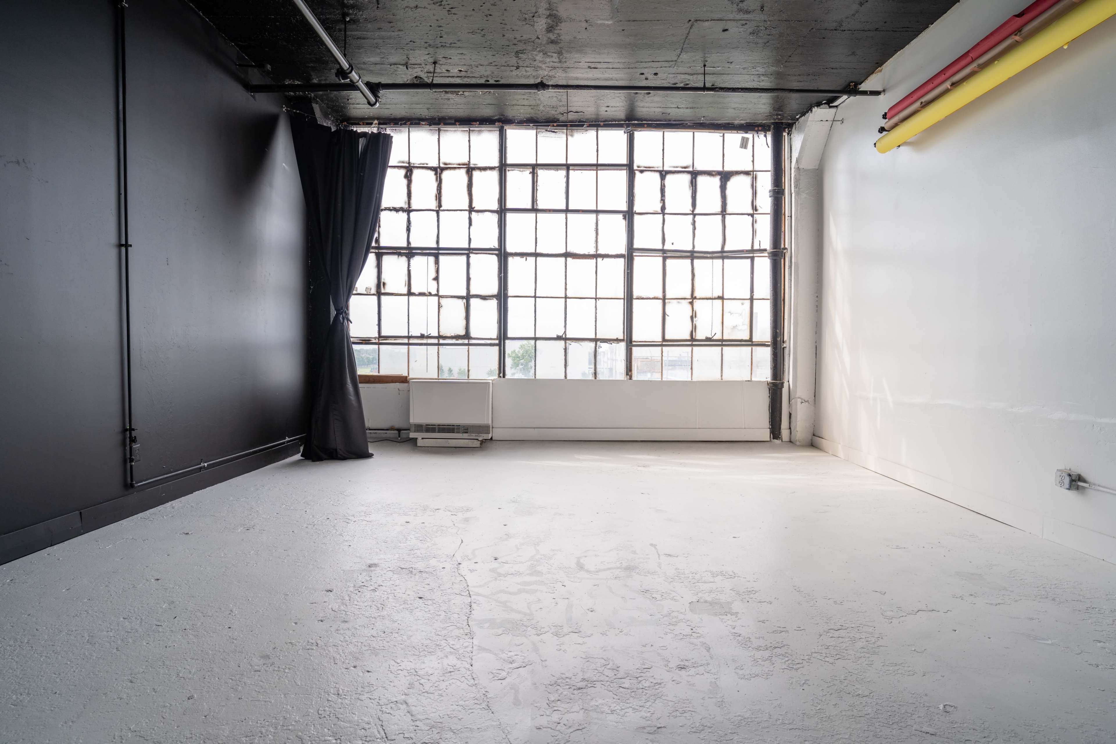 An empty room with a large industrial window, black walls, and a white floor.