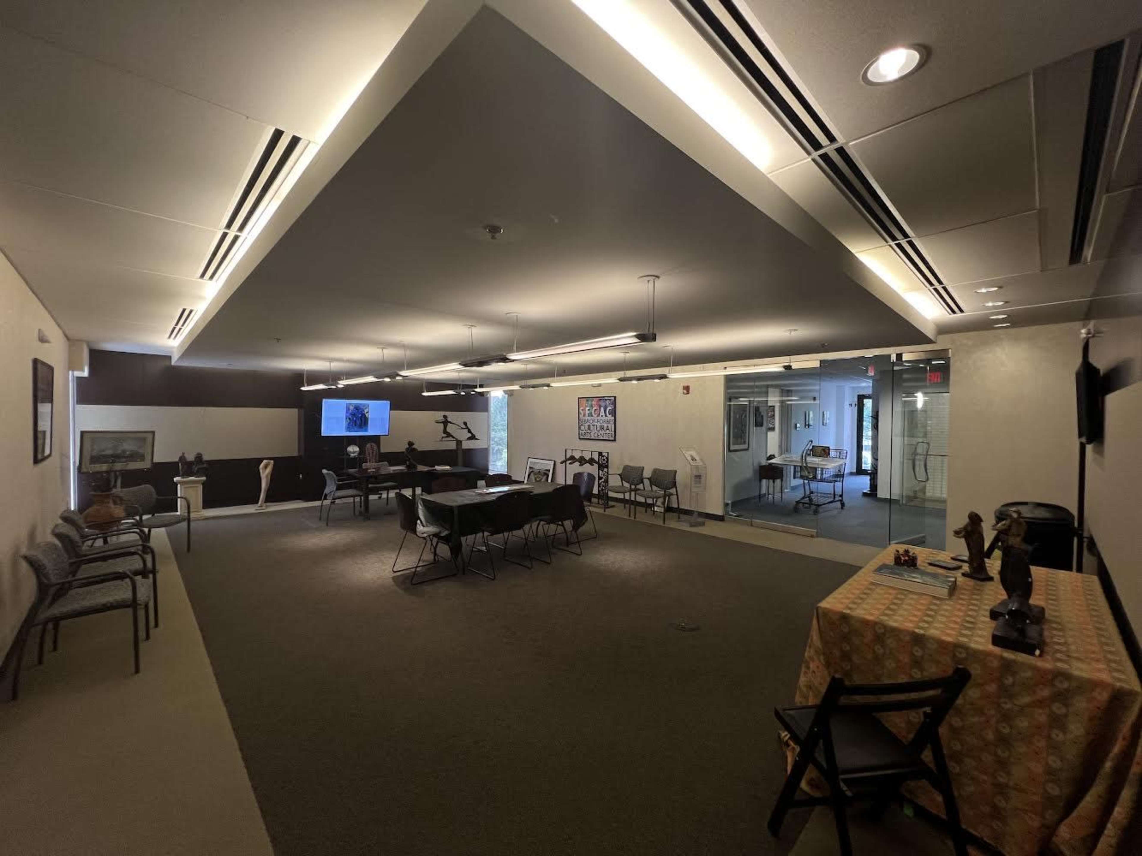 A spacious room with various seating arrangements, tables, and a screen at one end, indicating a meeting or gathering space.