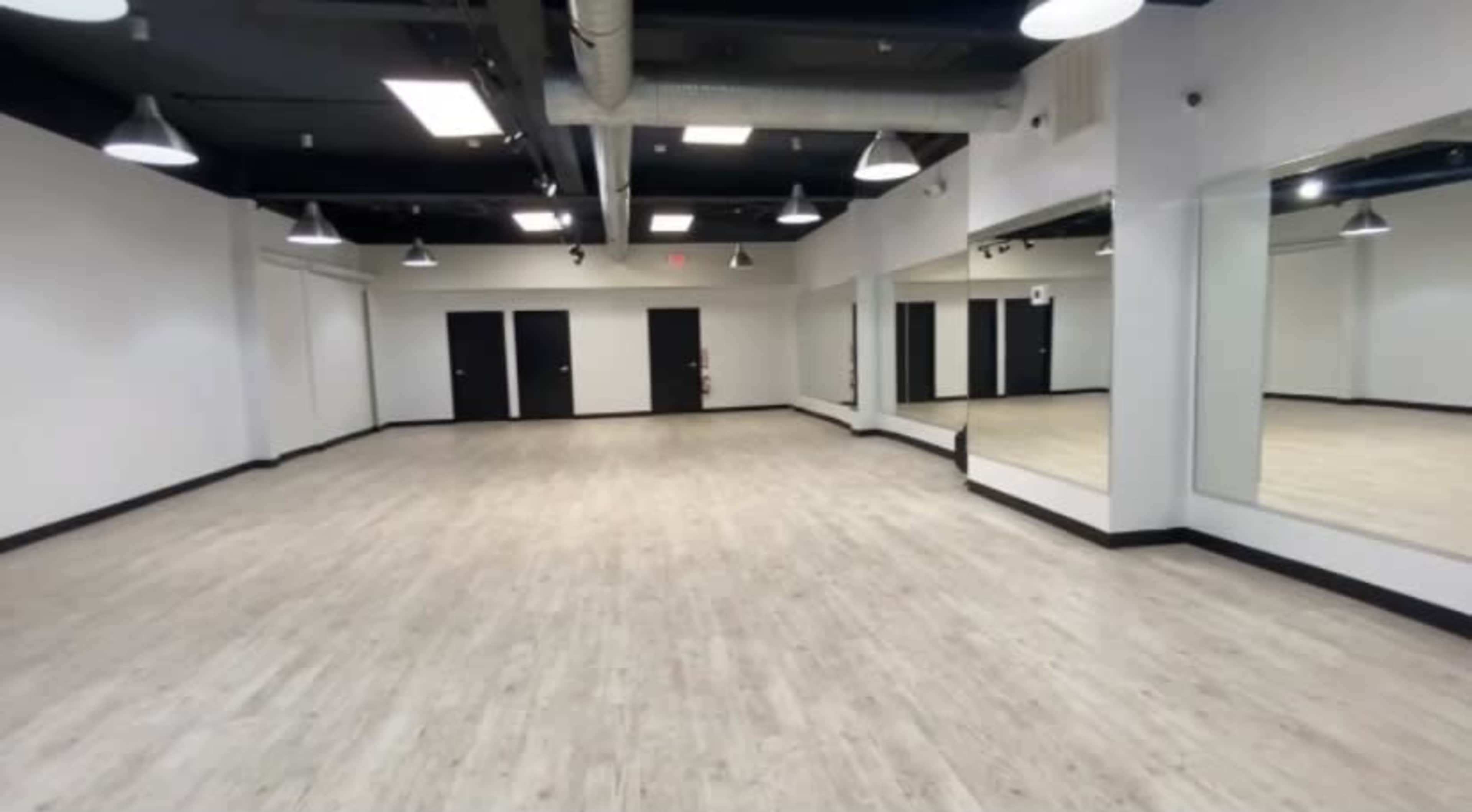An empty room with light-colored wooden flooring, white walls, and large mirrors on one side.
