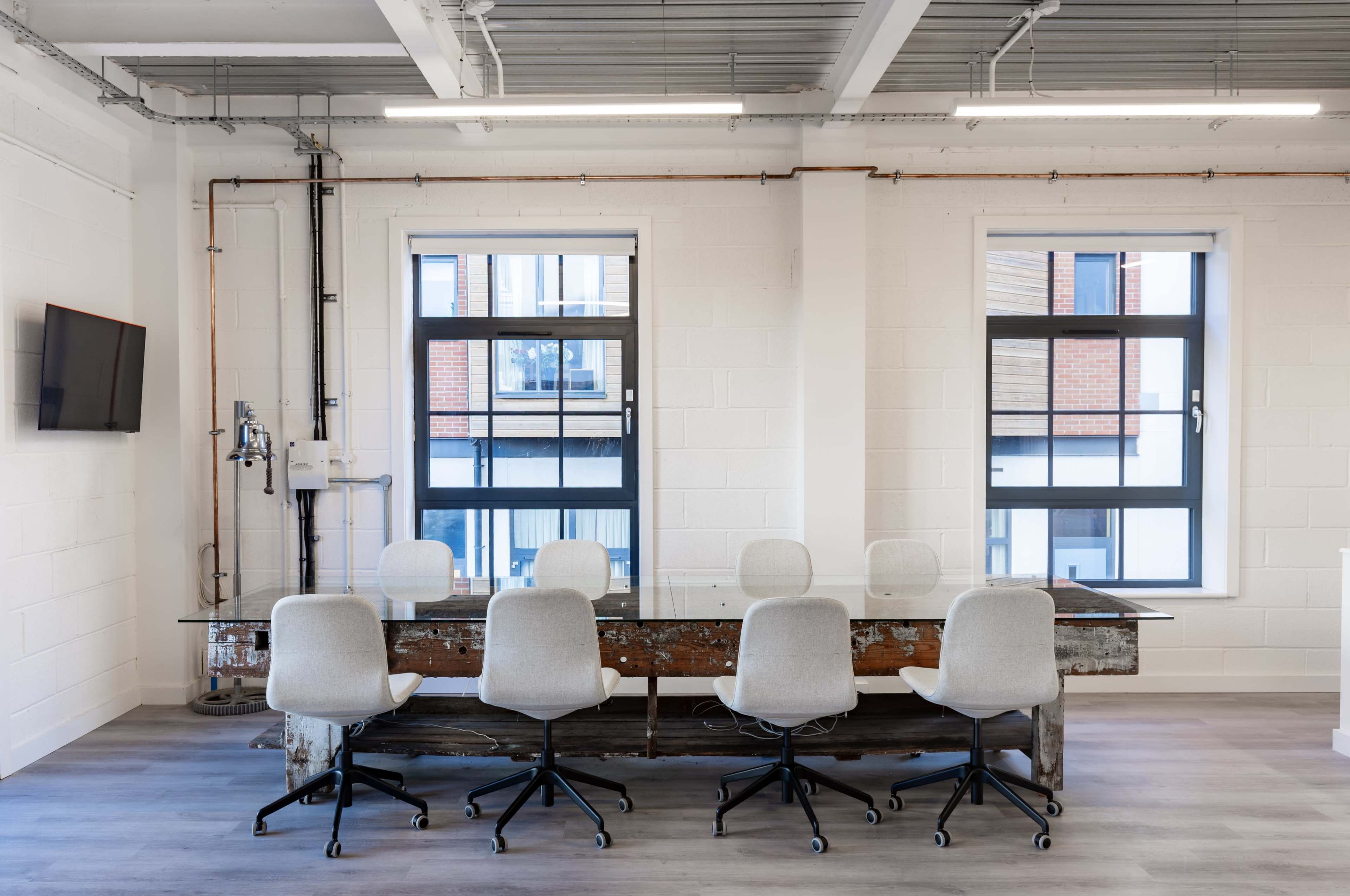 The image shows a modern conference room featuring a long wooden table with a glass top and six ergonomic office chairs arranged around it.