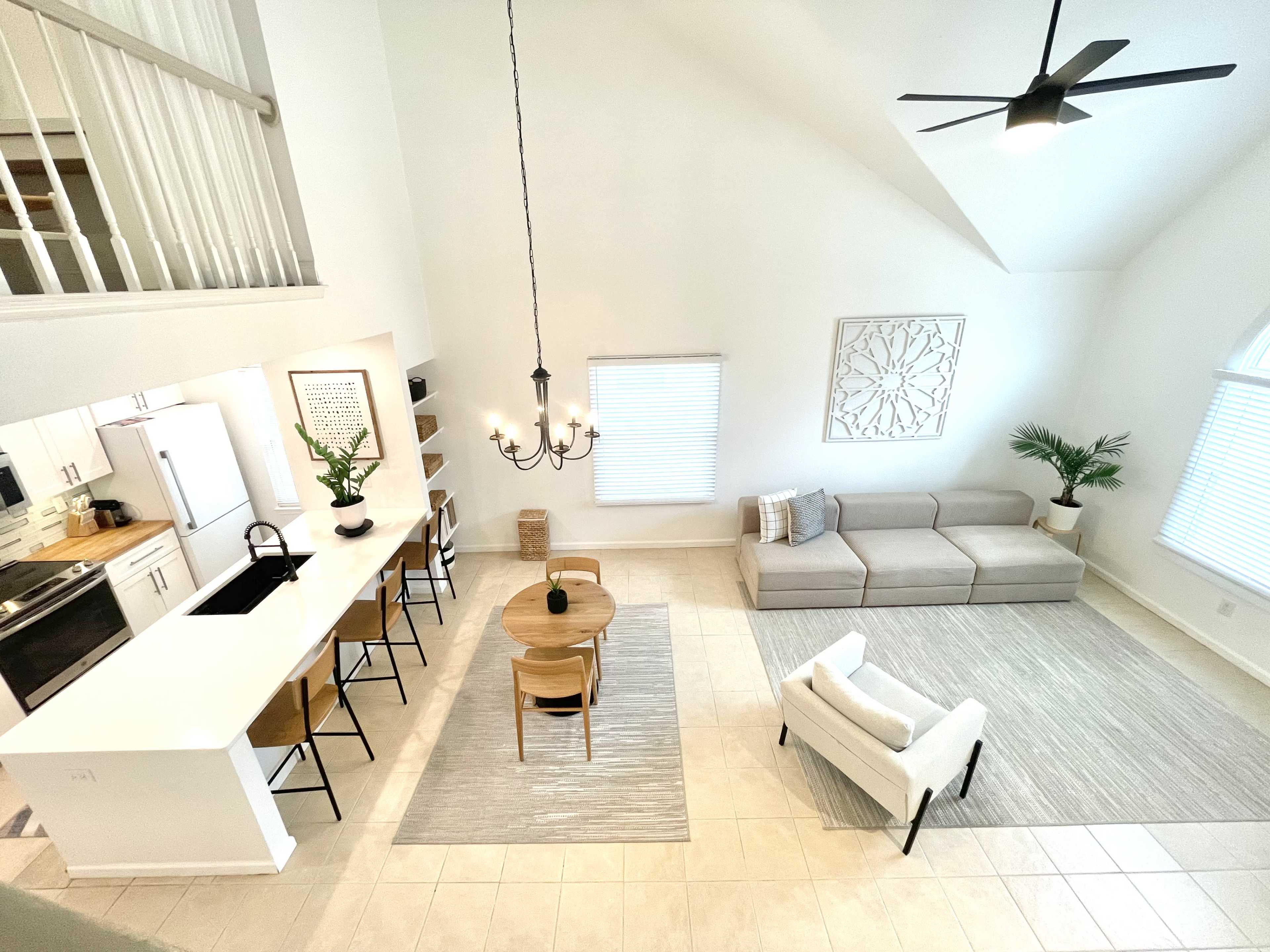 A spacious, modern living room and dining area with a neutral color palette, a large sectional sofa, a round dining table, and tall windows allowing natural light.