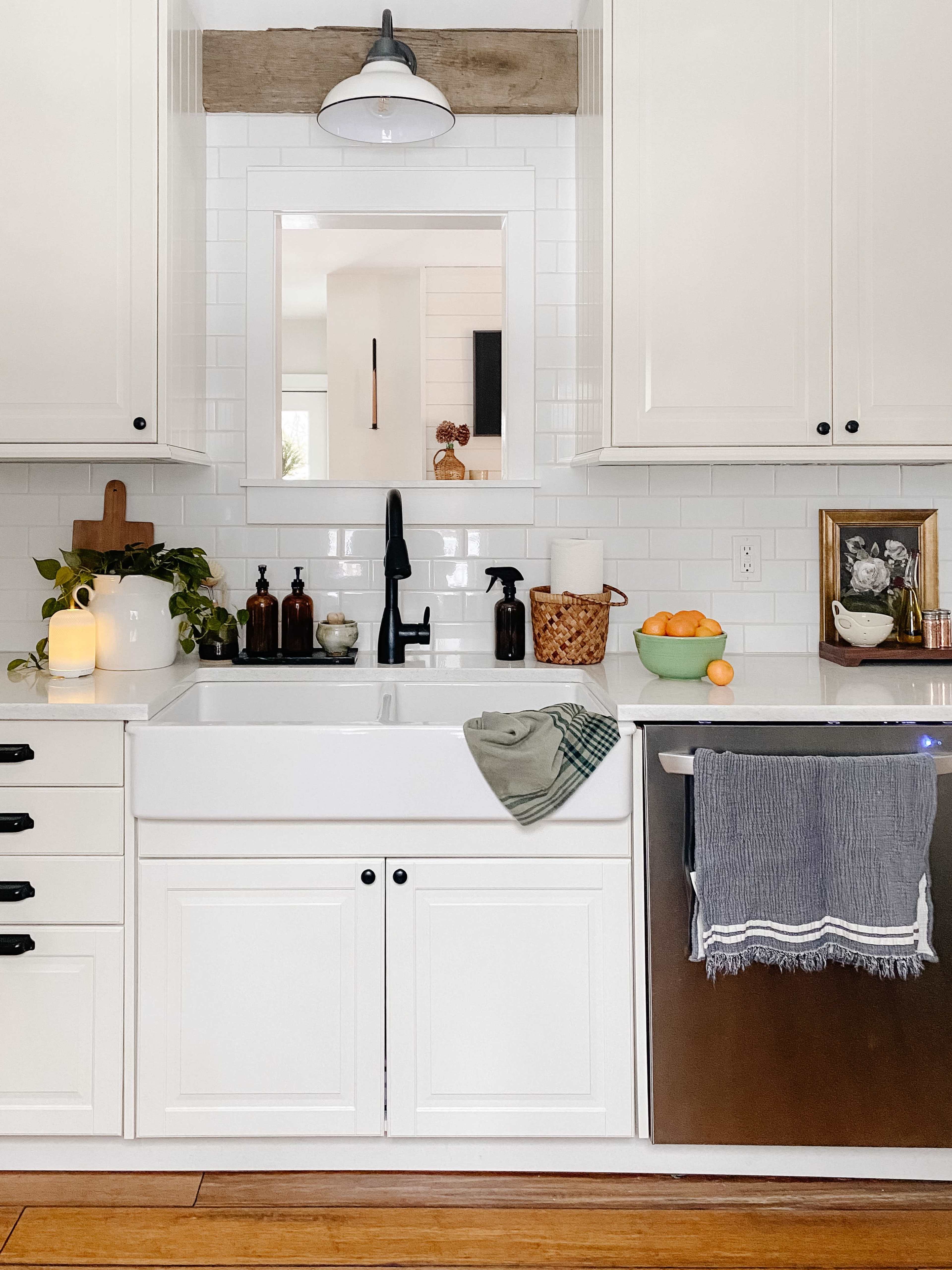 The kitchen features a farmhouse-style sink, white cabinetry, and a mirror framed with wood above the countertop.