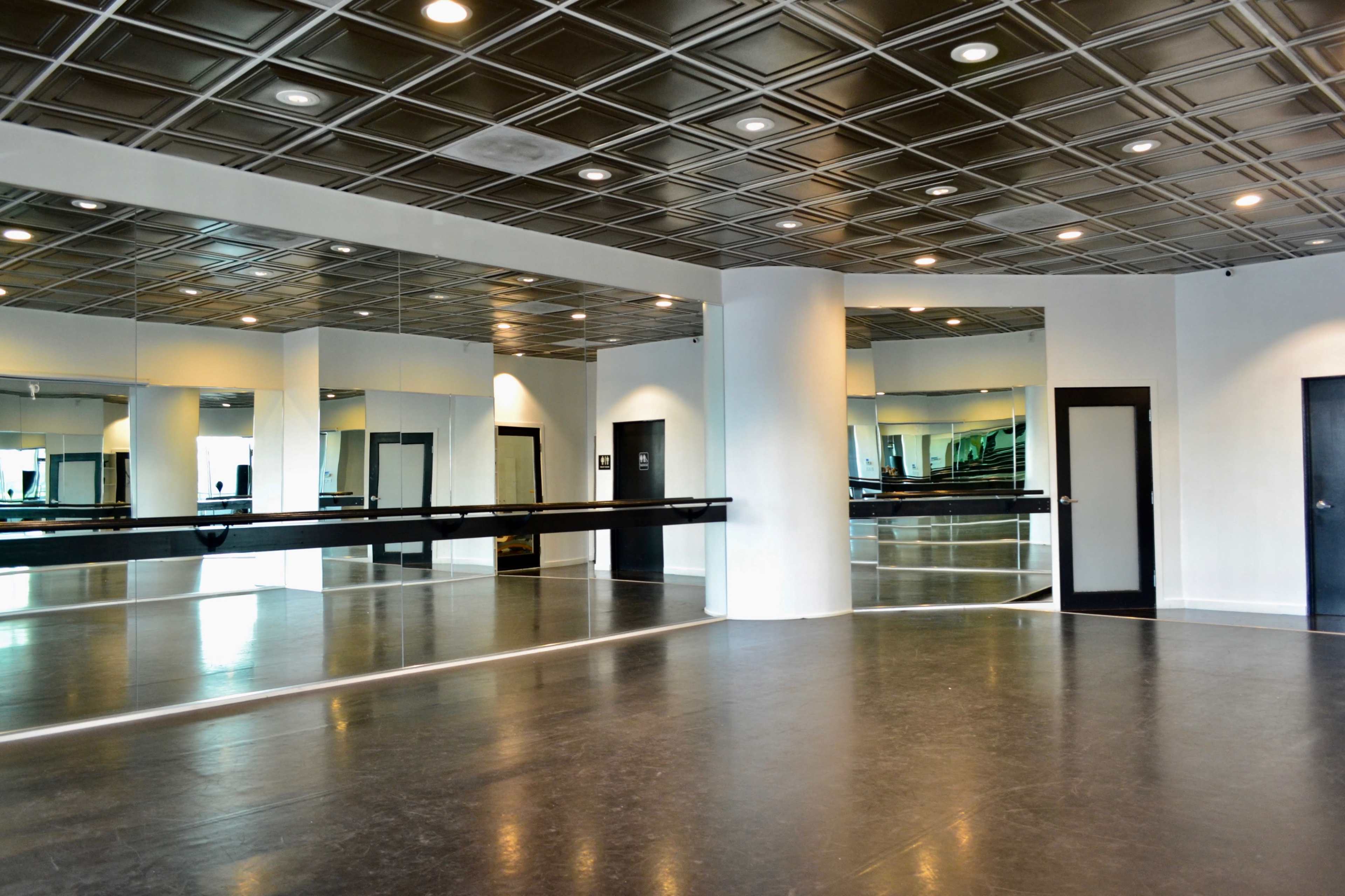 A spacious dance studio features mirrored walls, polished floors, and a black barre along one side.
