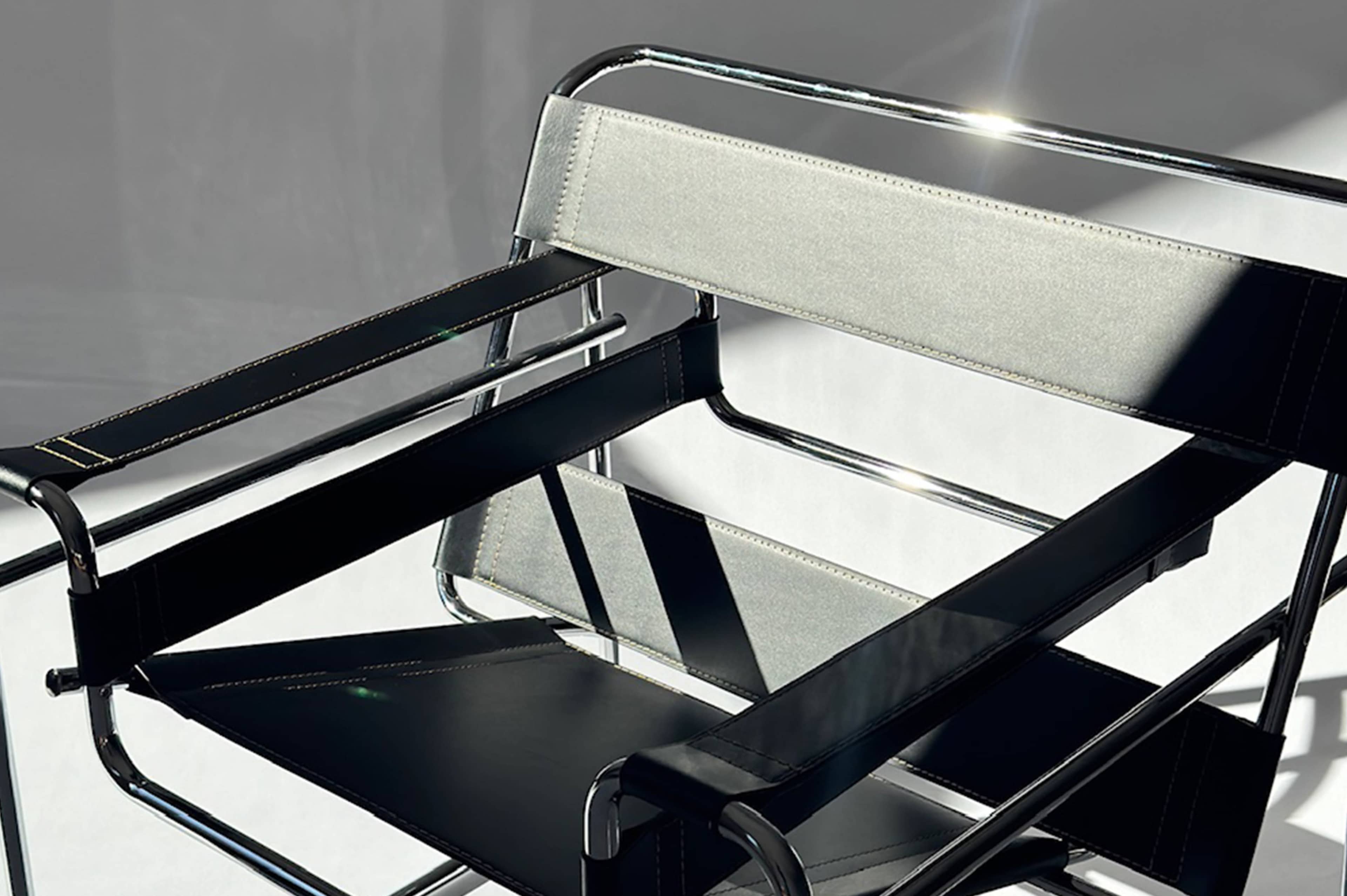 The image shows a modern chair with a chrome frame and black fabric seats, positioned against a light backdrop.