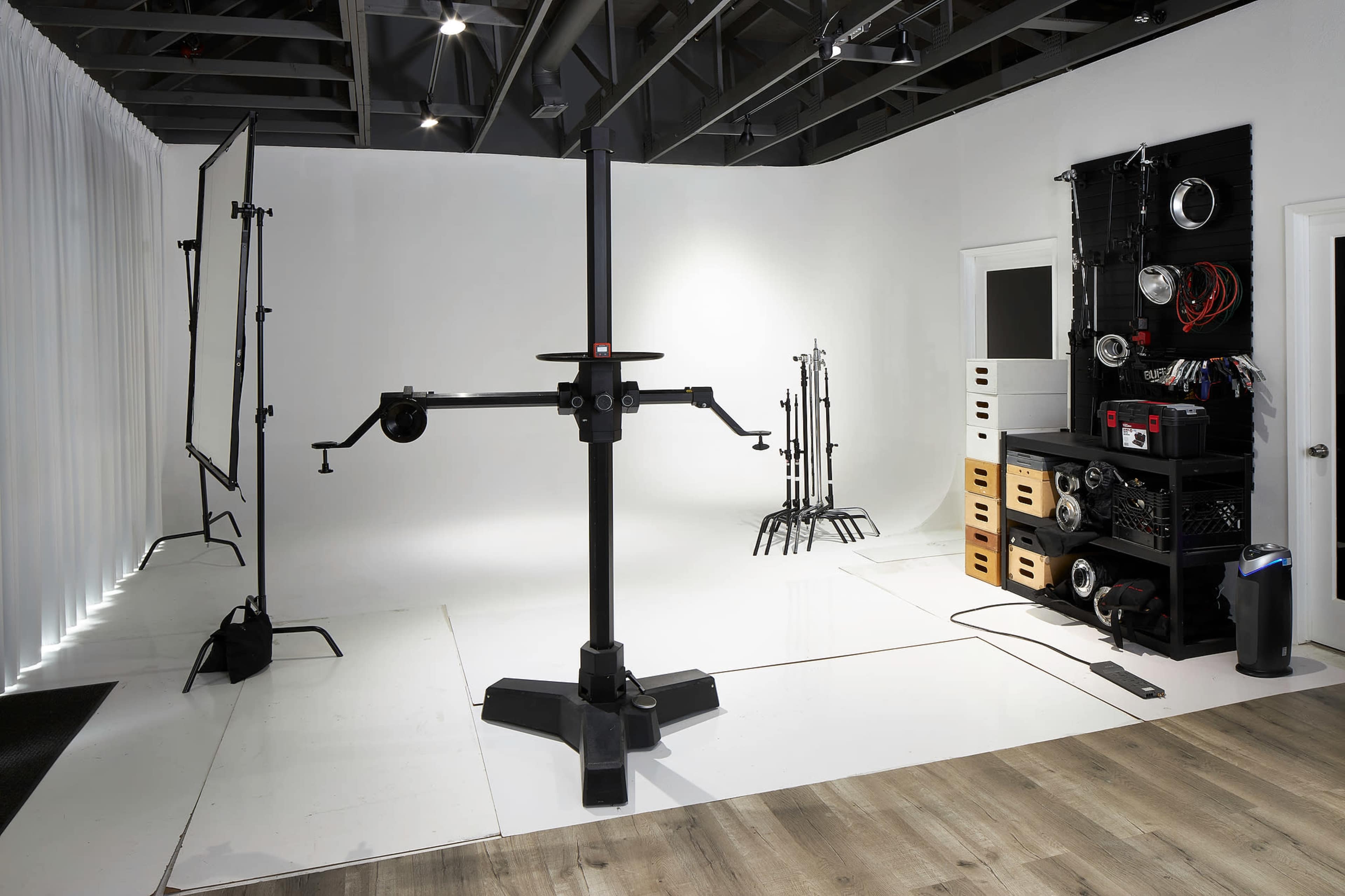 A photography studio with a central tripod, various light stands, backdrop support, and organizational furniture for equipment along the wall.