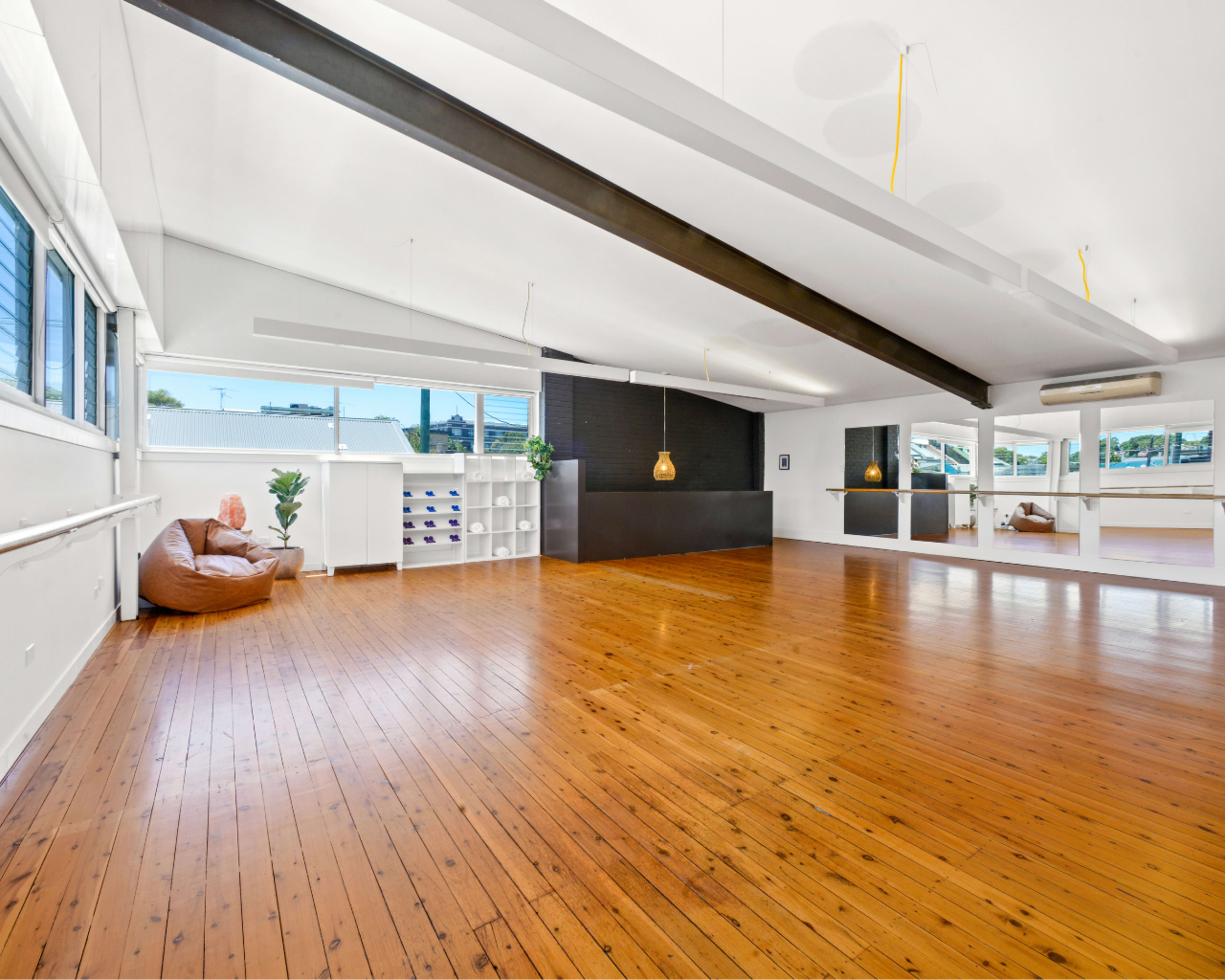 A spacious interior with wooden flooring, large windows, and a minimalistic design featuring a seating area and an island counter.