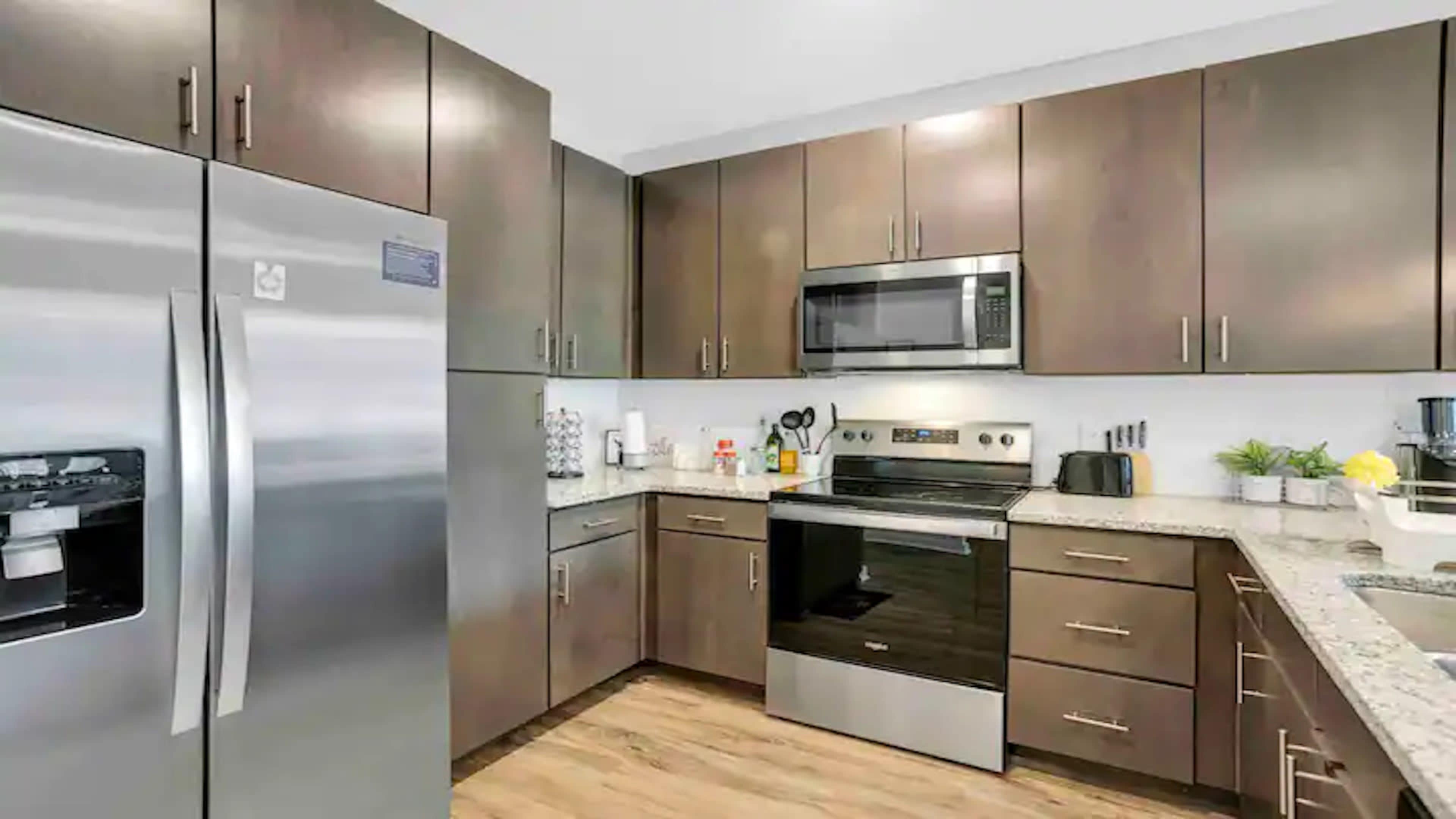 The image shows a modern kitchen with stainless steel appliances, including a refrigerator and microwave, and wooden cabinetry.
