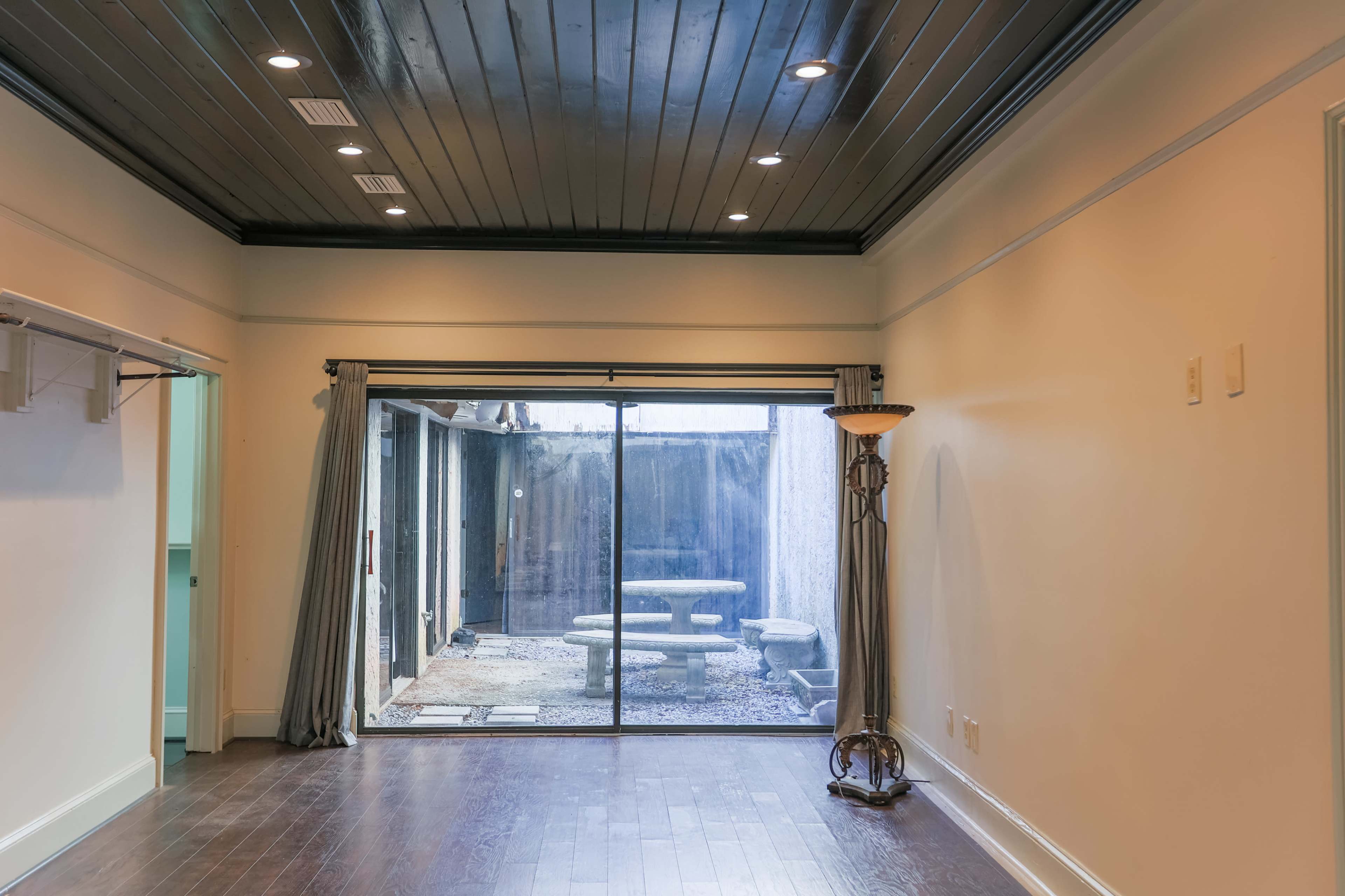 A room with hardwood flooring and a large sliding glass door leading to a backyard with a stone table and paved area.